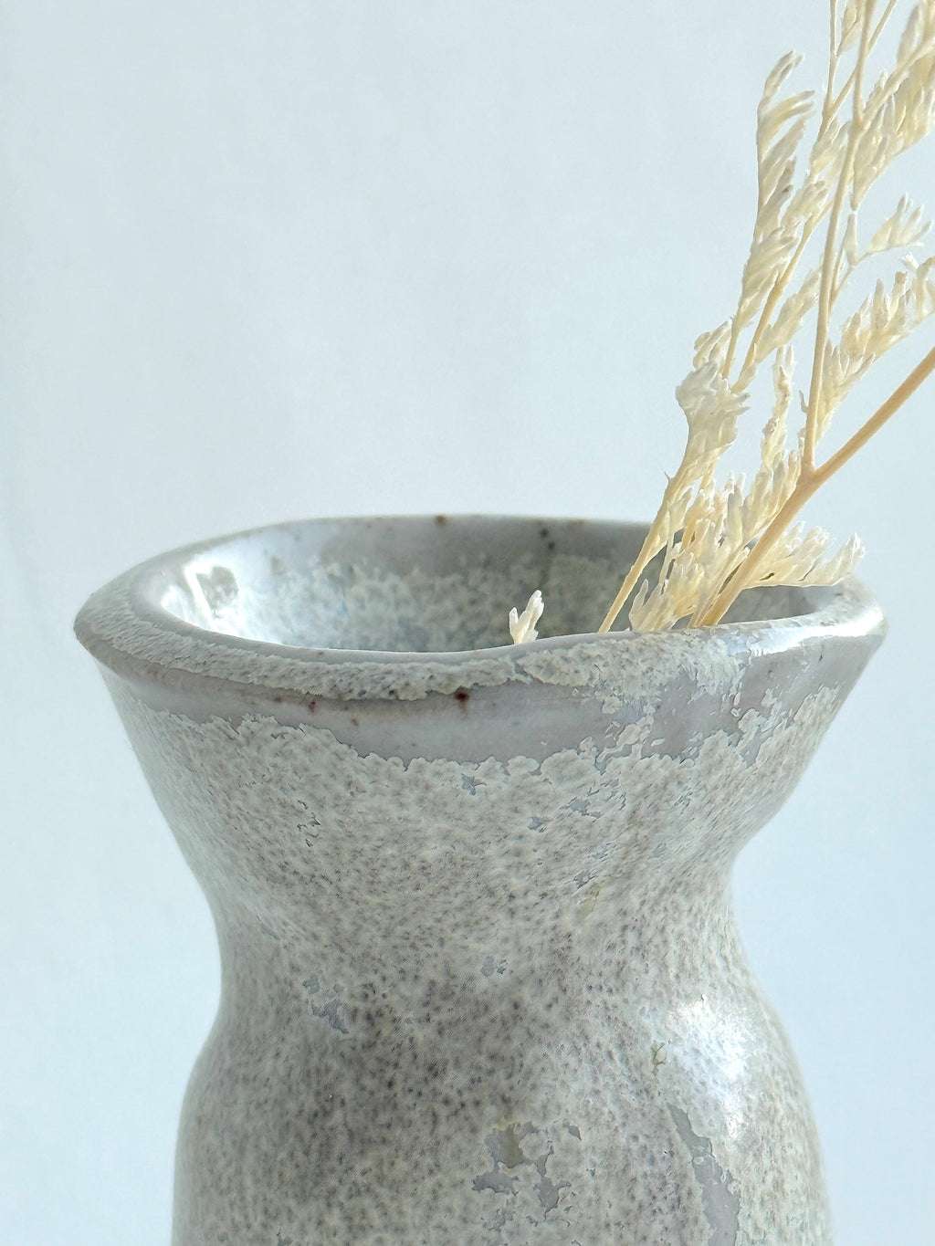 Gray ceramic vase with textured surface holding dried plants on a light gray background