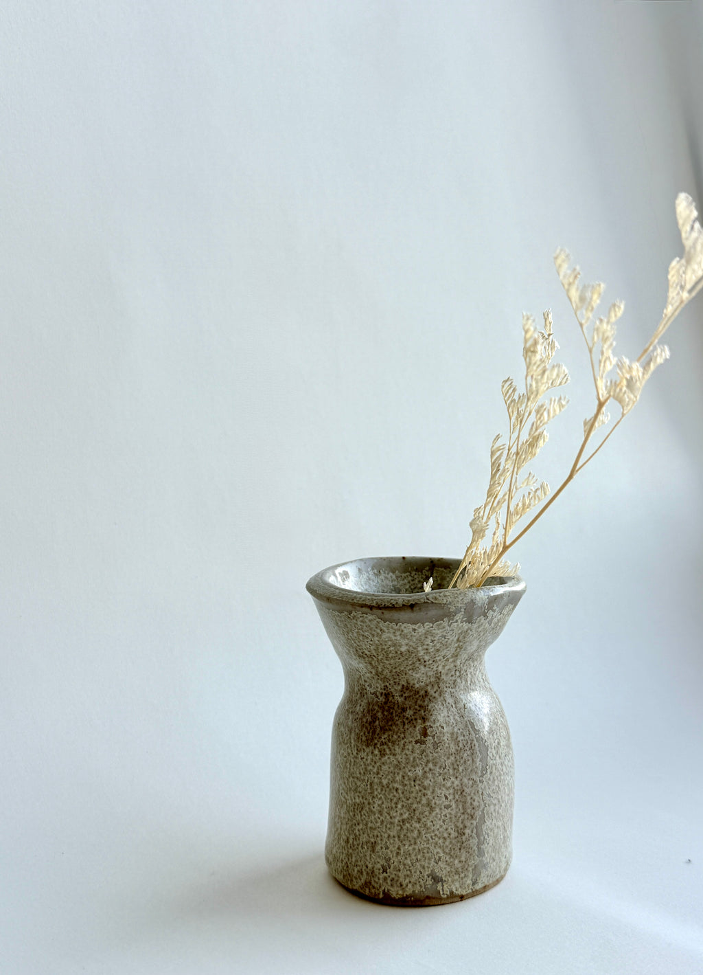 Handbuilt stone-textured ceramic mini vase with mottled beige and grey glaze and soft hourglass shape