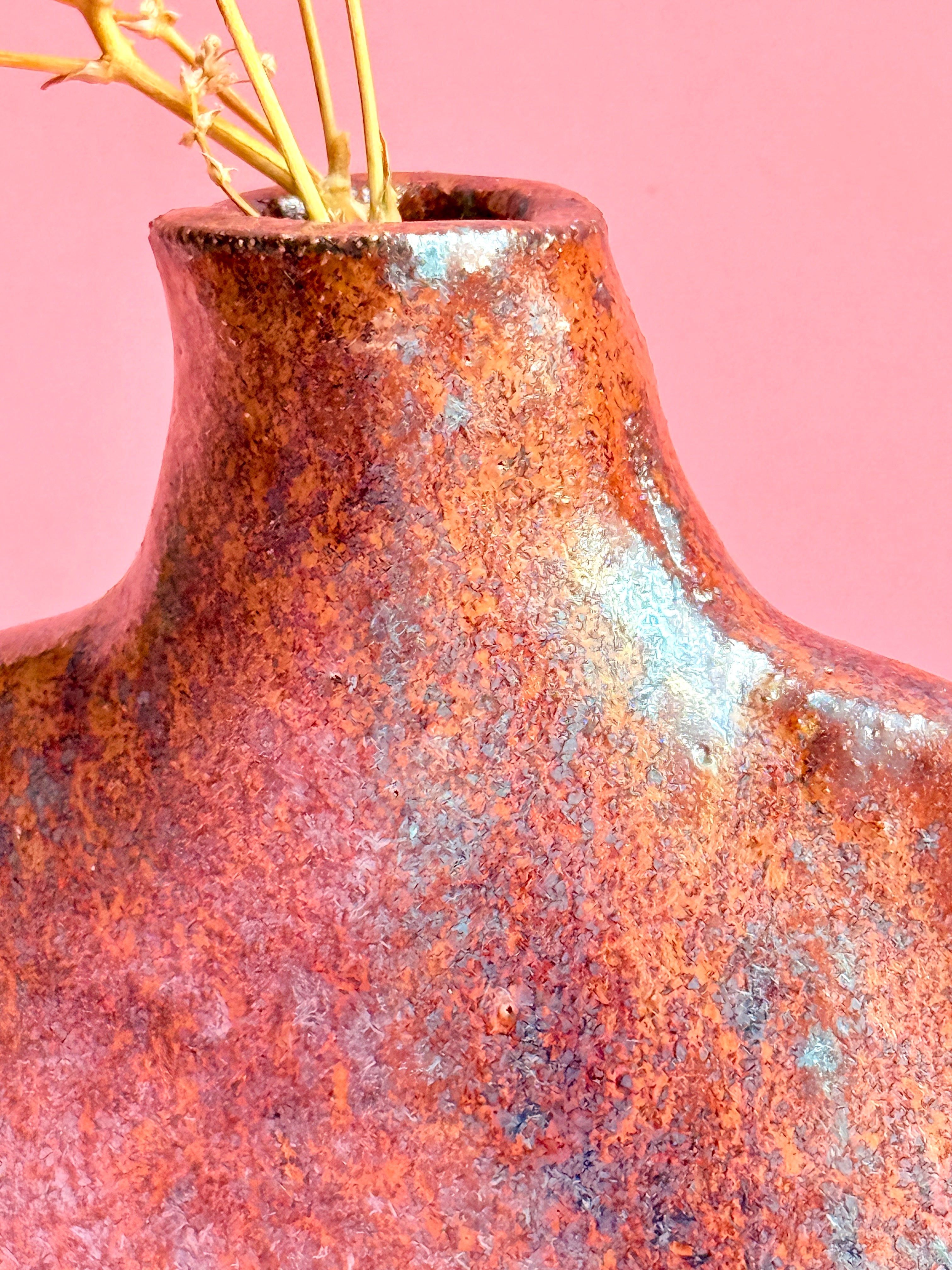 Rust-colored ceramic vase with a textured surface on a pink background