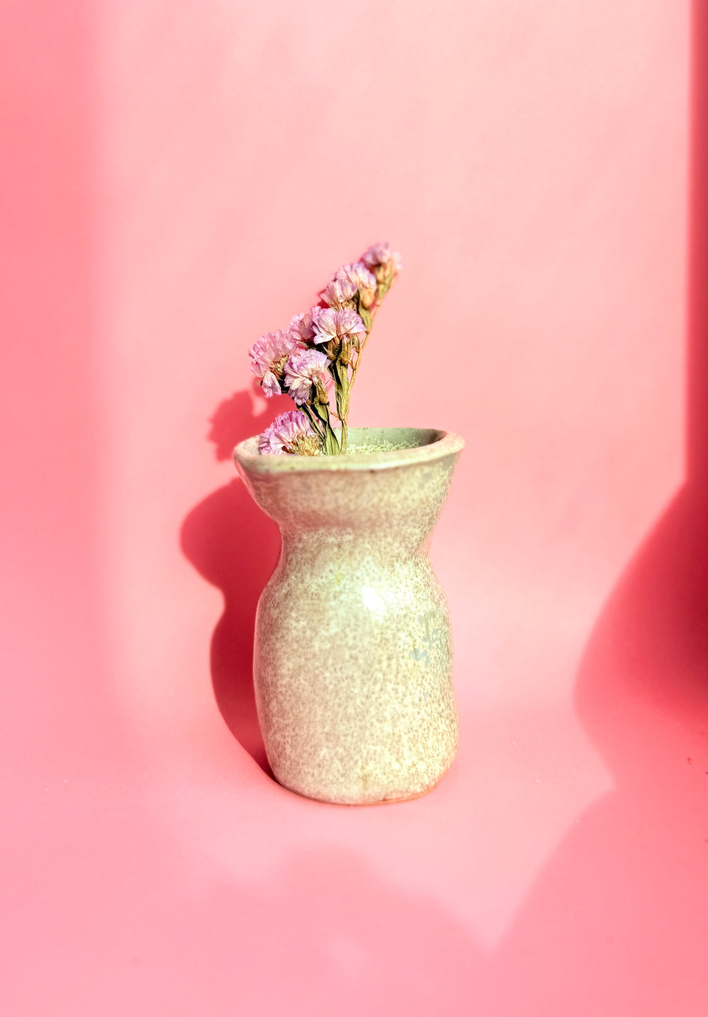 Green textured vase with flowers on a pink background