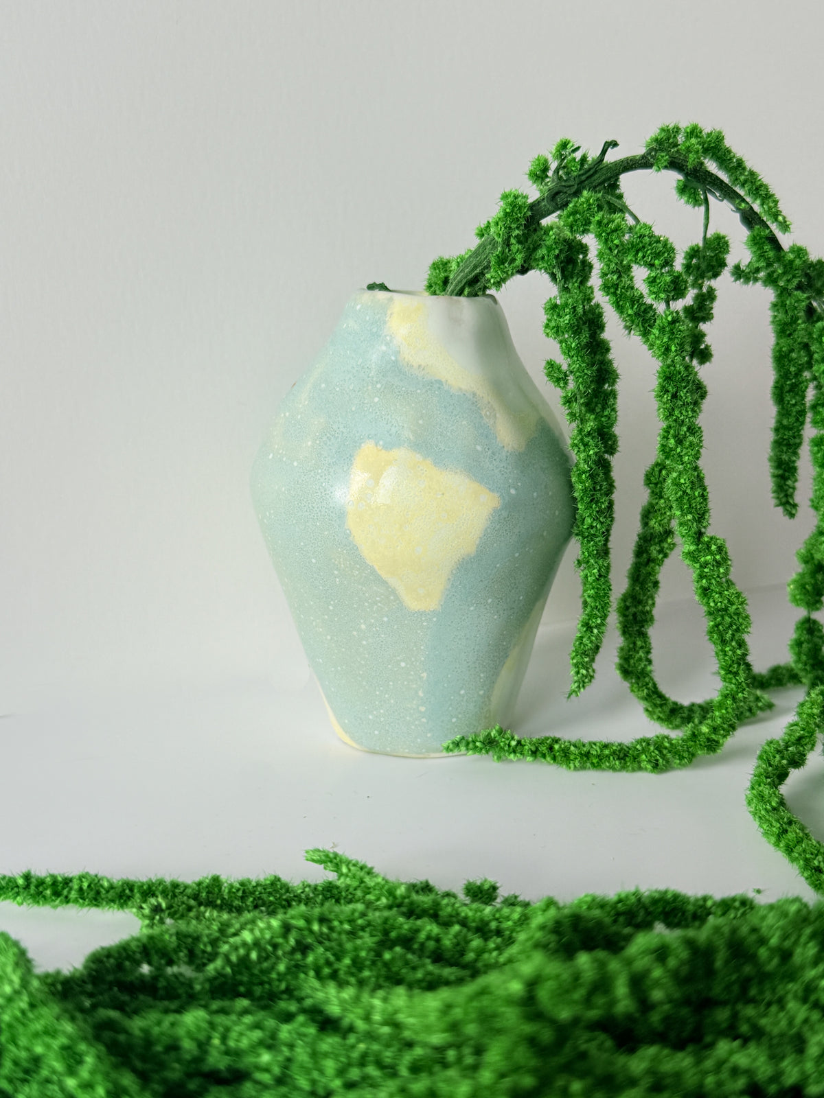 Tiny handbuilt blue and butter yellow ceramic bud vase with bright green dried amaranth spilling over the rim