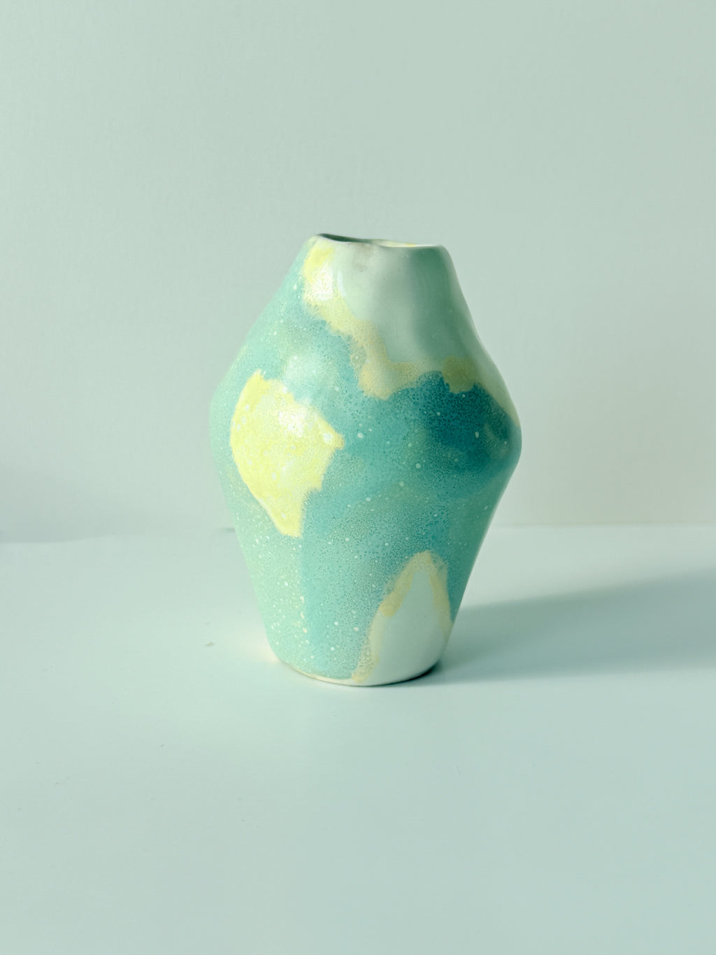 Side view of a tiny one of a kind blue and butter yellow handbuilt bud vase with a speckled glaze