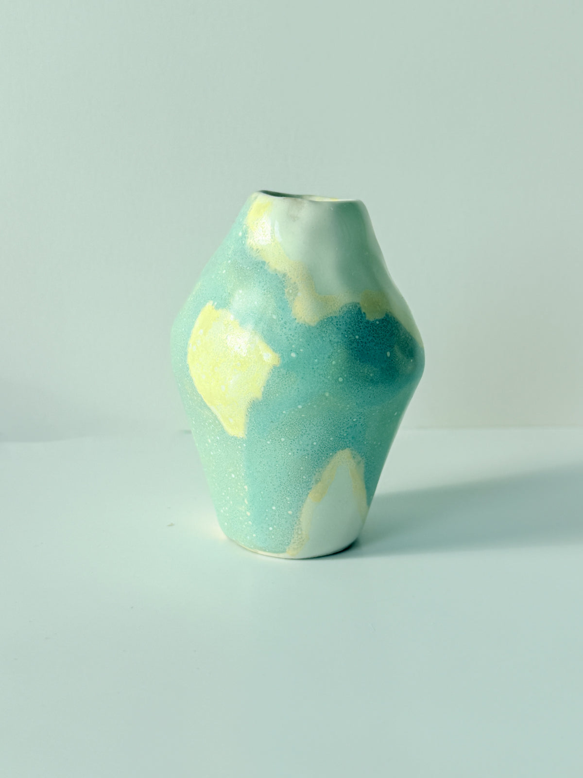 Side view of a tiny one of a kind blue and butter yellow handbuilt bud vase with a speckled glaze