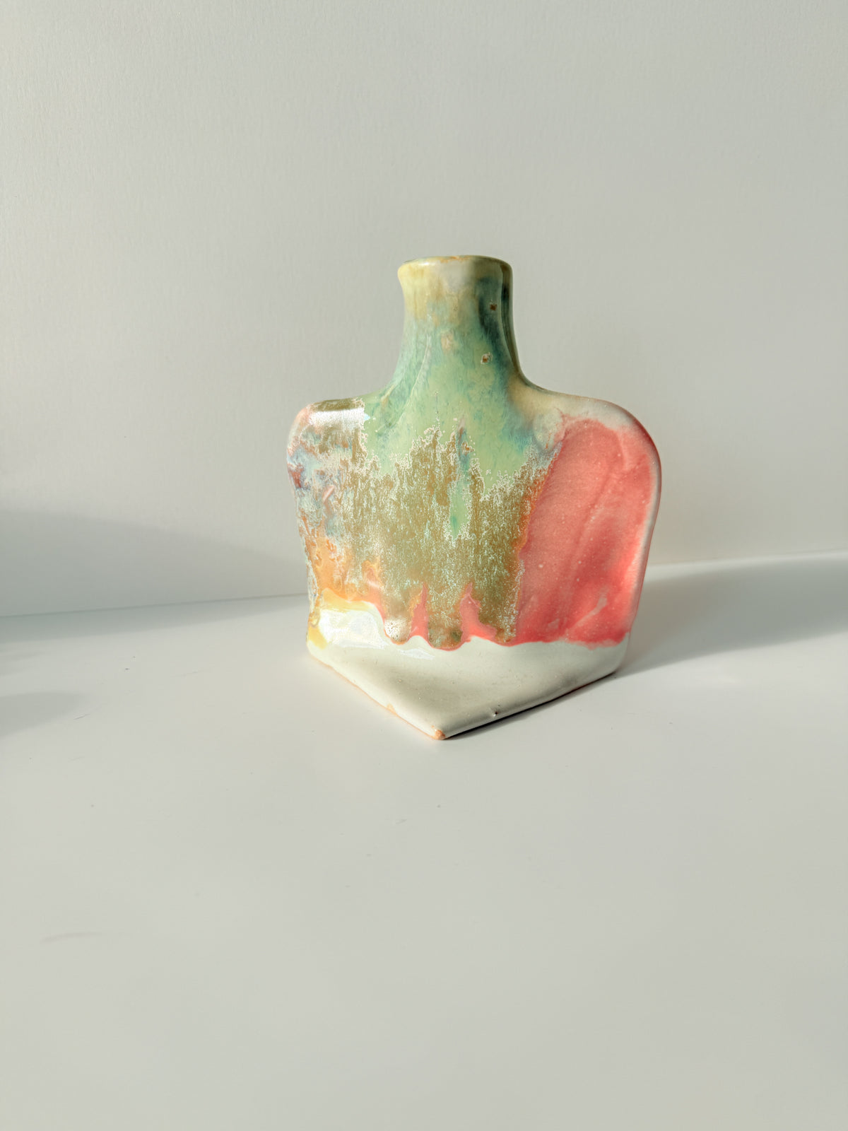 A small handmade ceramic vase with a wide, rounded body and a narrow neck, decorated with a multicolor glaze featuring pink, green, gold, and white.