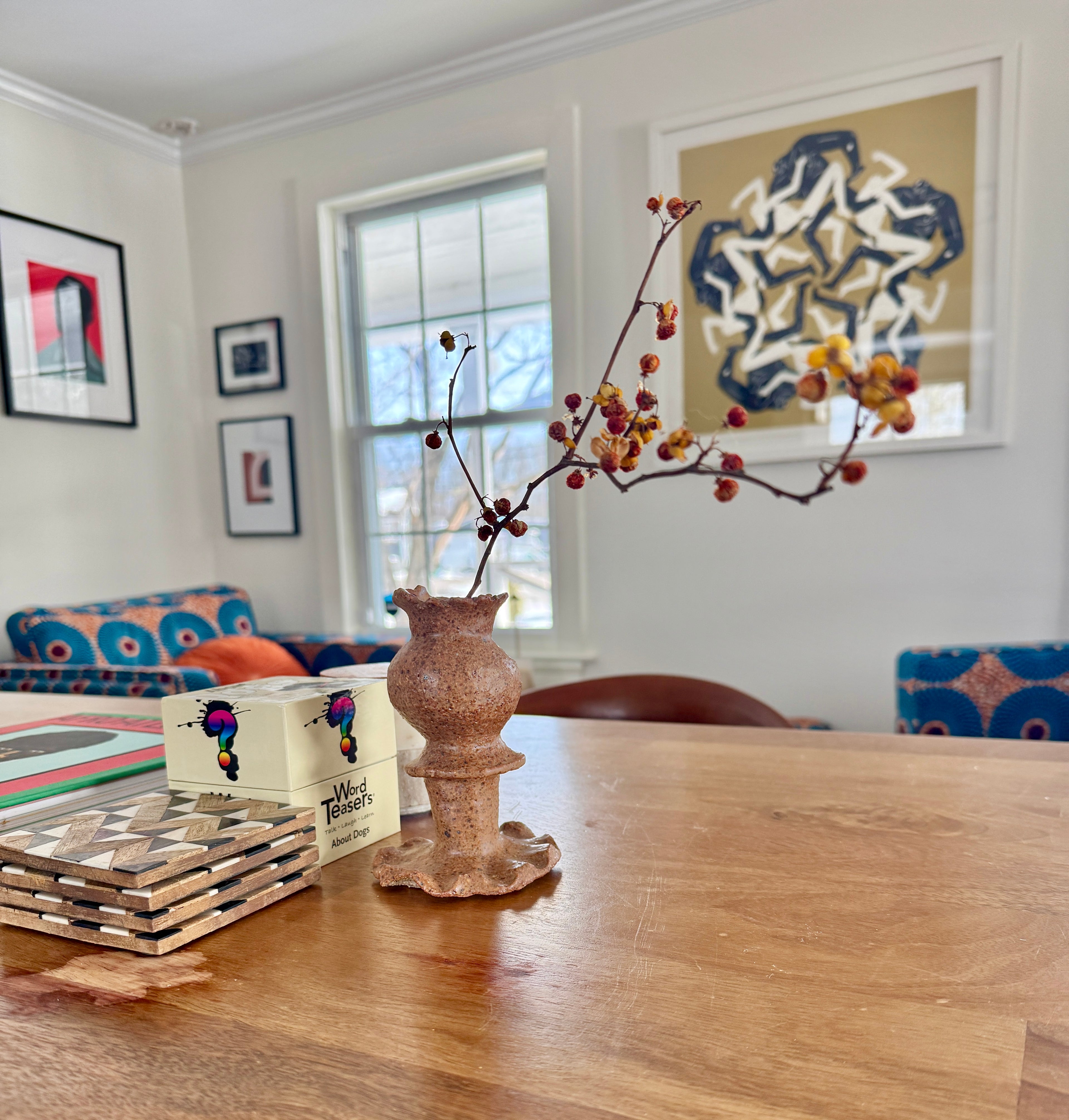 Dining room with a wooden table, vase with branches, and colorful chairs.
