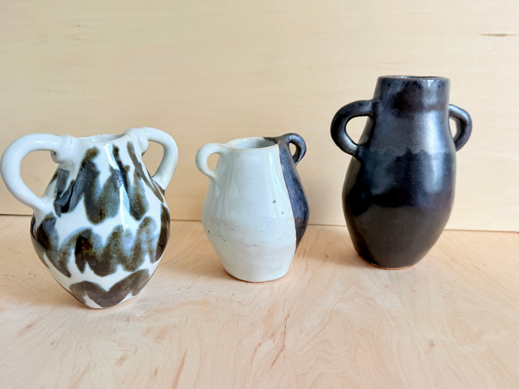 Three ceramic vases of different designs on a wooden surface with a beige background