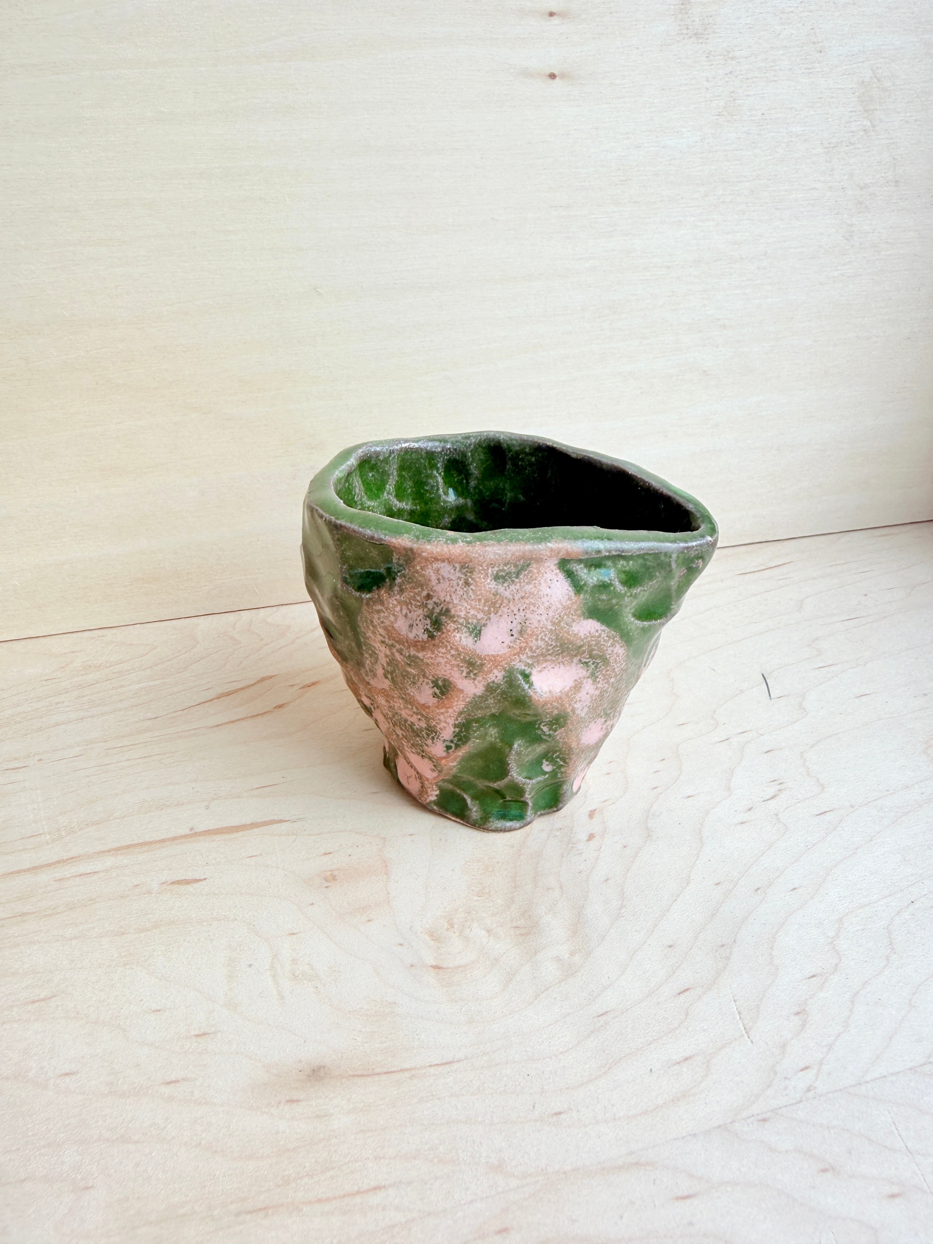 Ceramic vase with green and pink marbled pattern on a light wooden floor.
