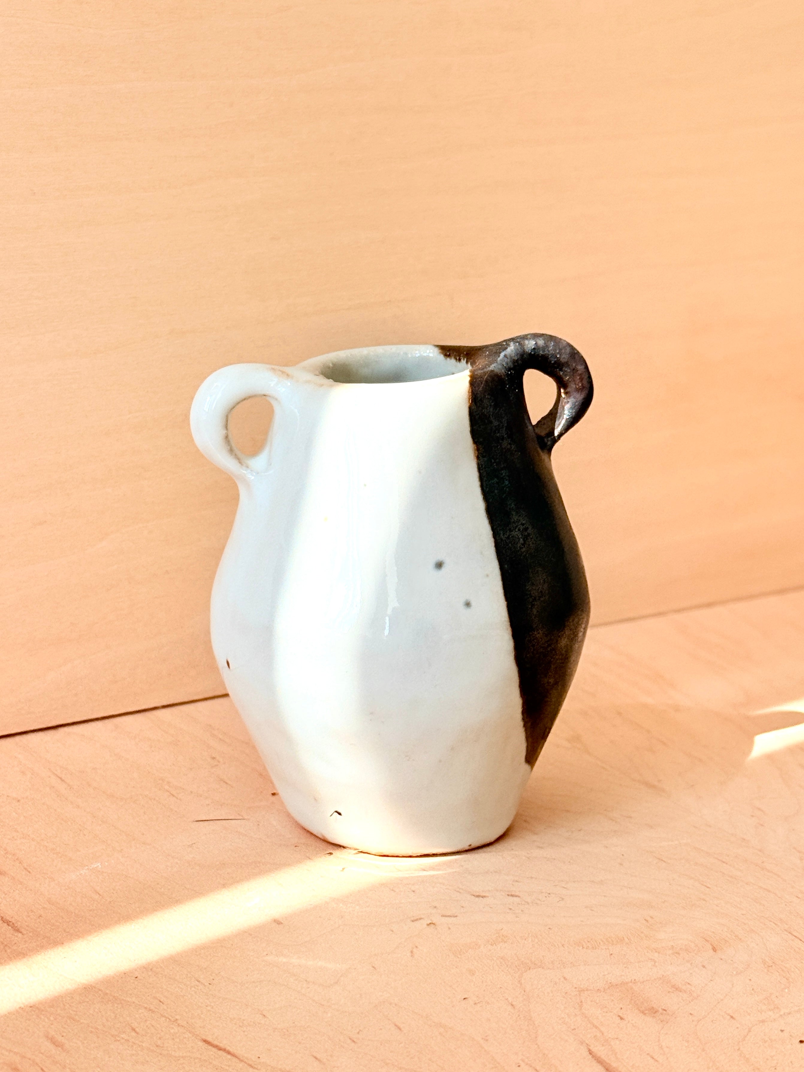 White ceramic pitcher with black handle on a beige background