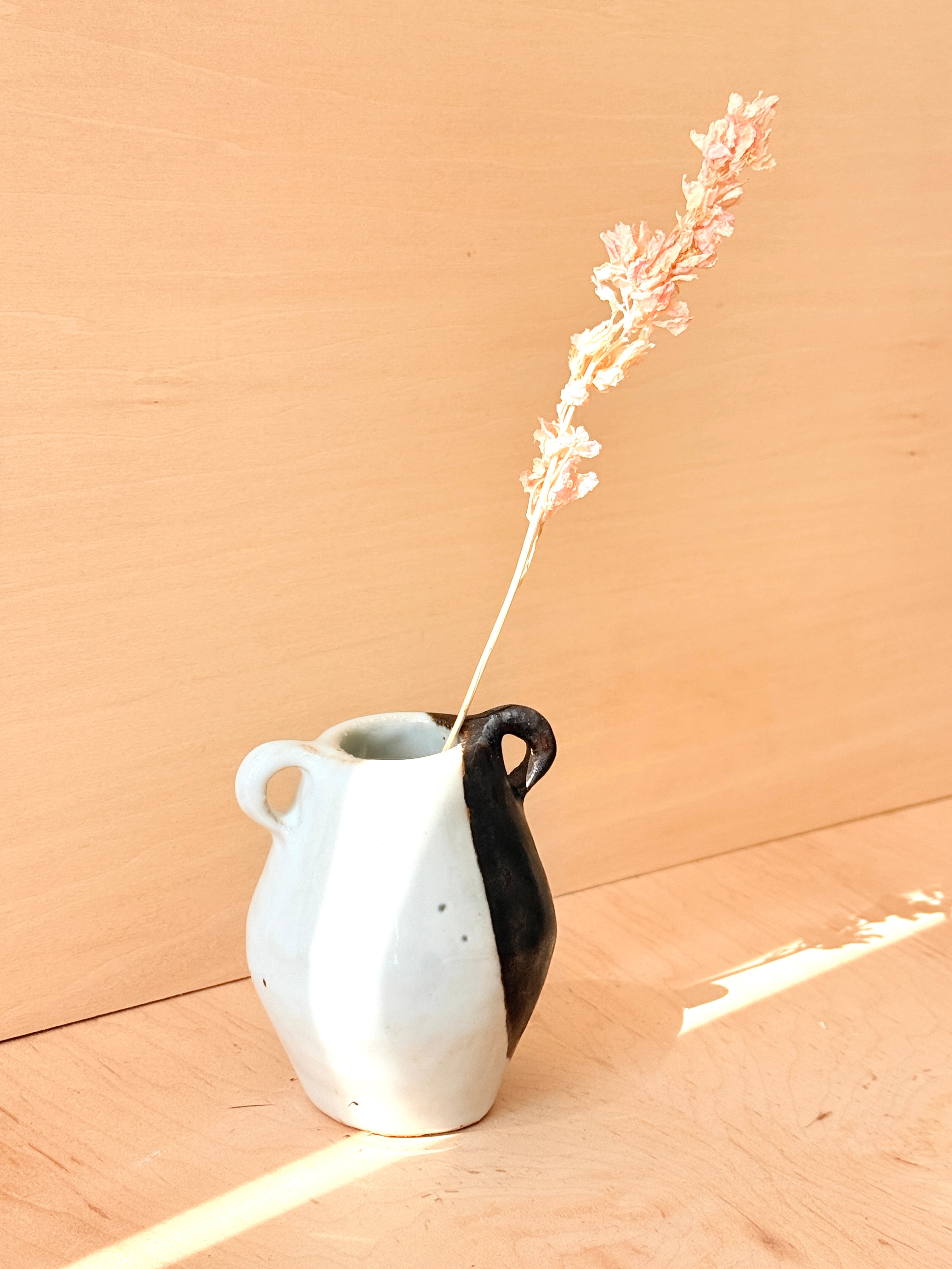 White ceramic pitcher with black handle holding a dried flower against a beige background