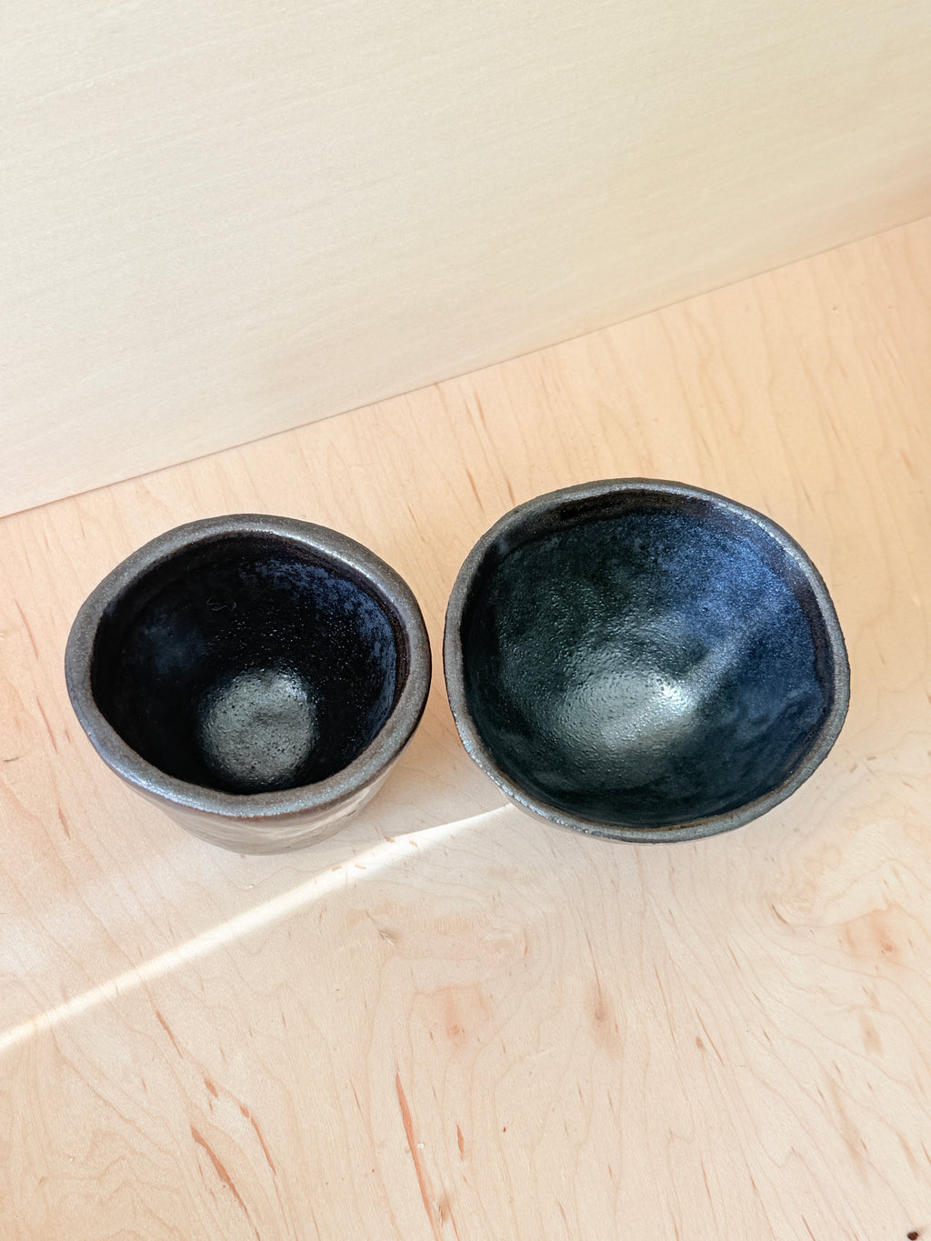 Two black ceramic bowls on a light wooden surface