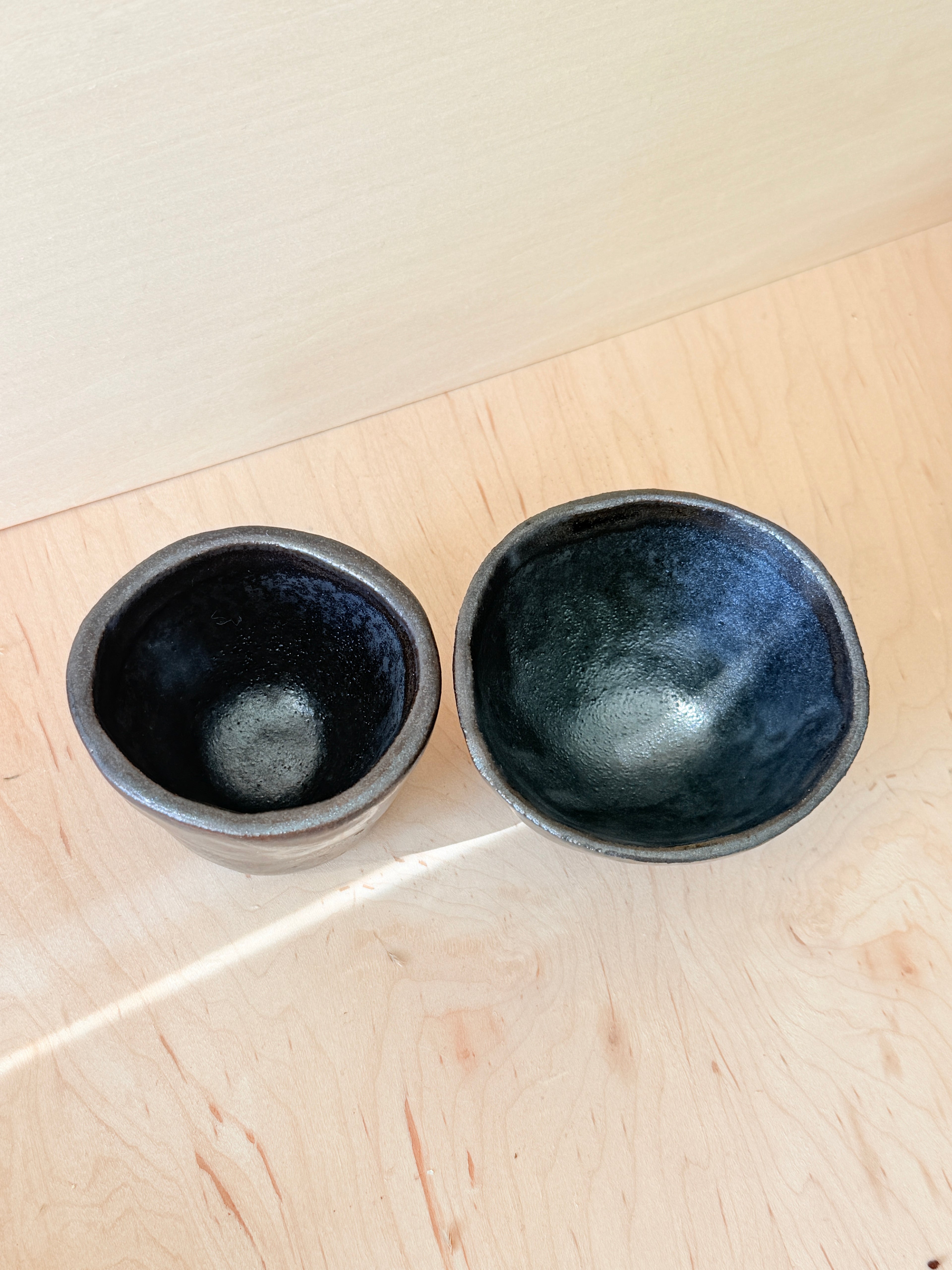 Two black ceramic bowls on a light wooden surface