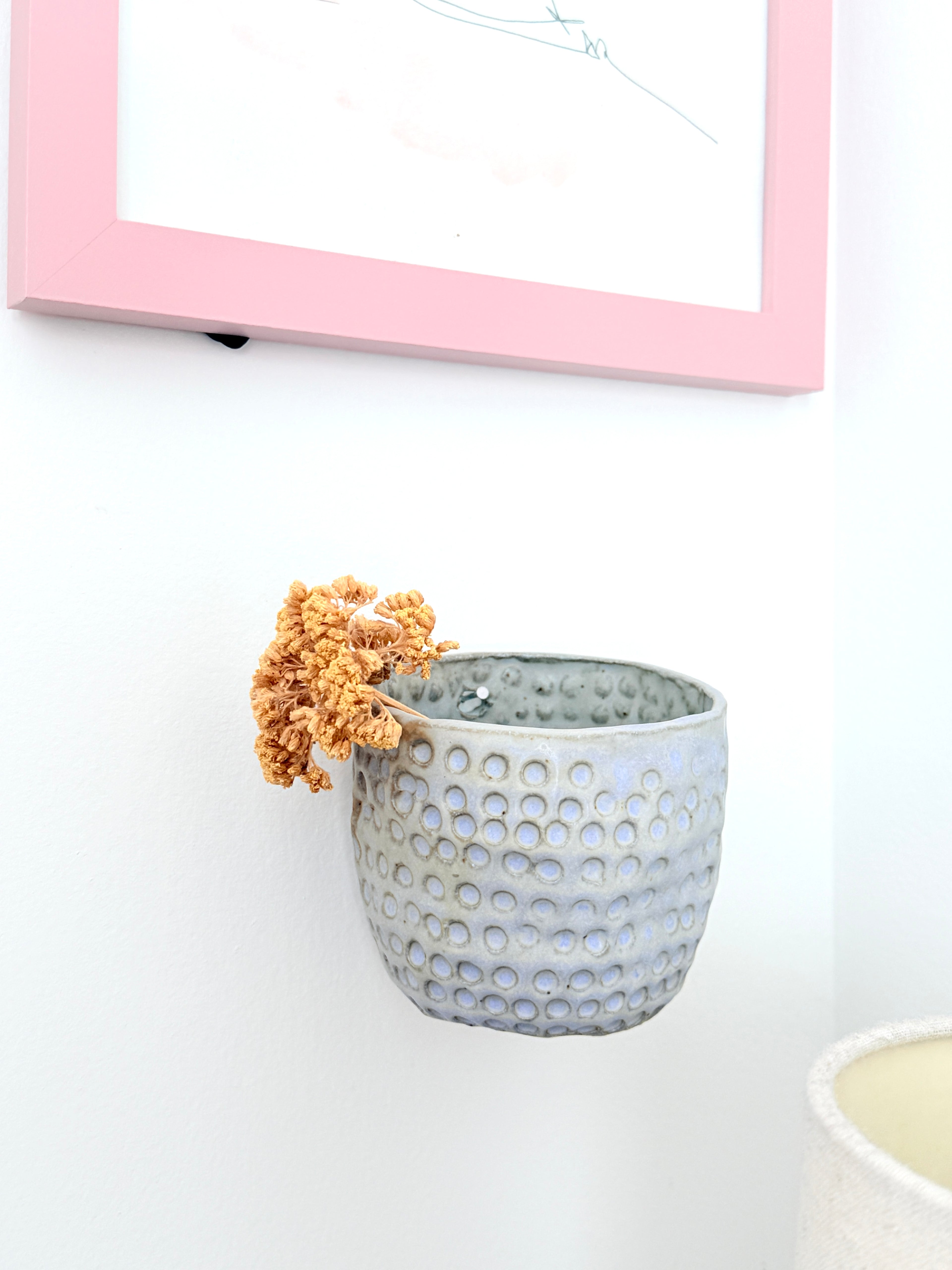 Gray textured pot with dried flowers on a white surface with a pink frame in the background