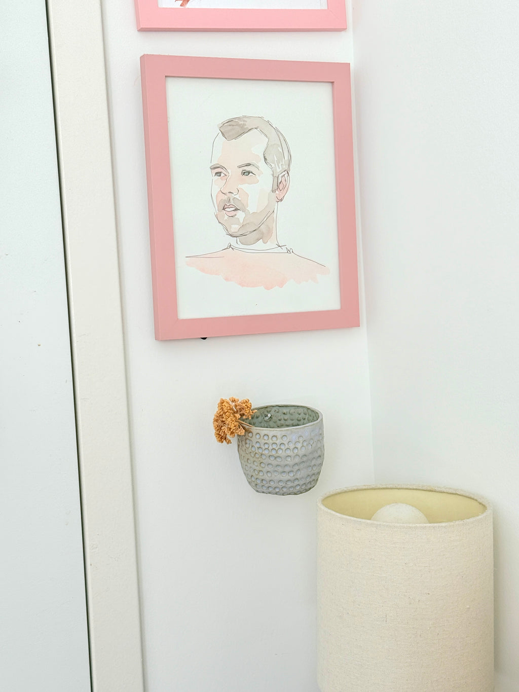 Framed portrait on a wall with a small plant and lamp in the foreground.