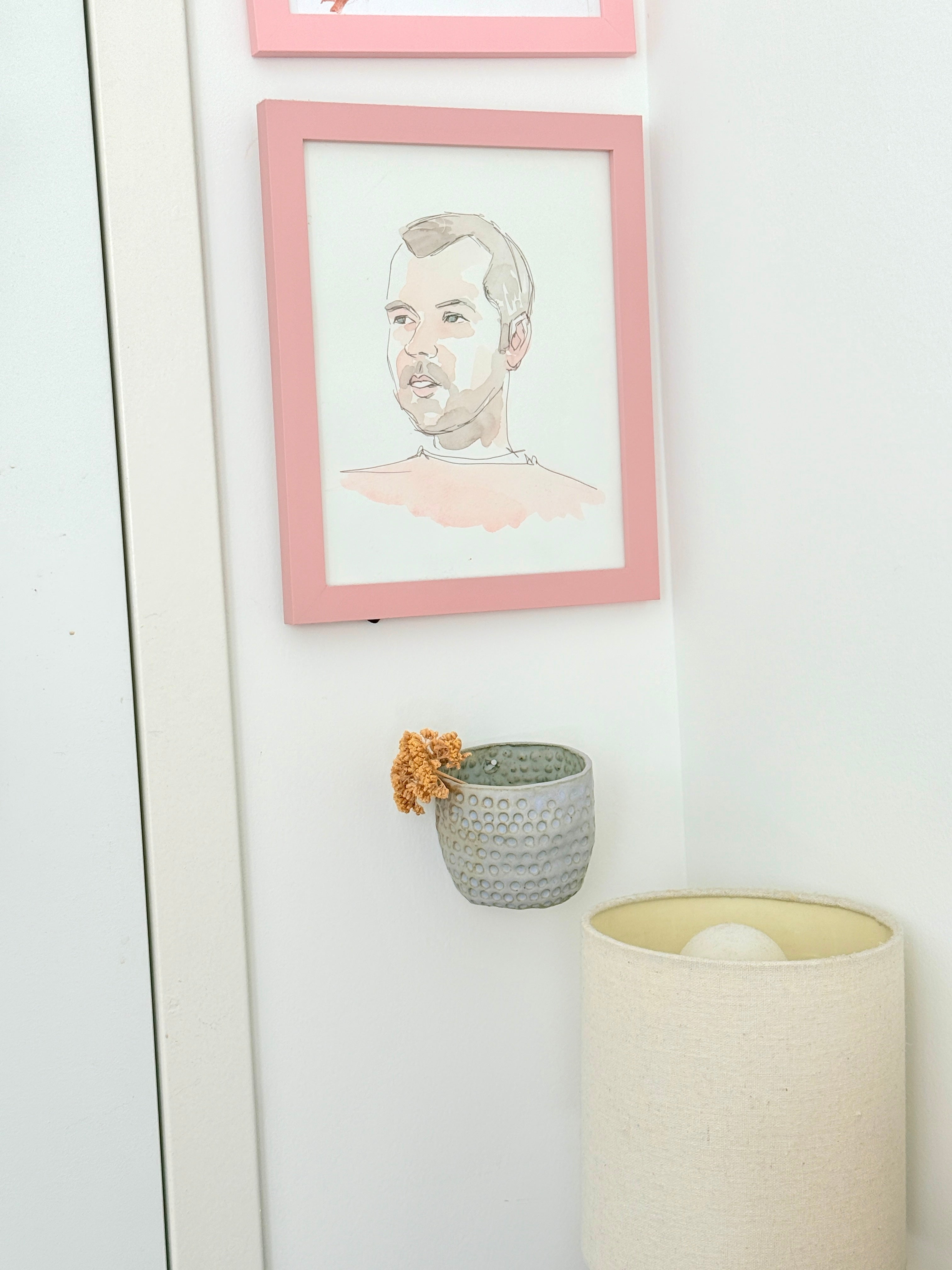 Framed portrait on a wall with a small plant and lamp in the foreground.