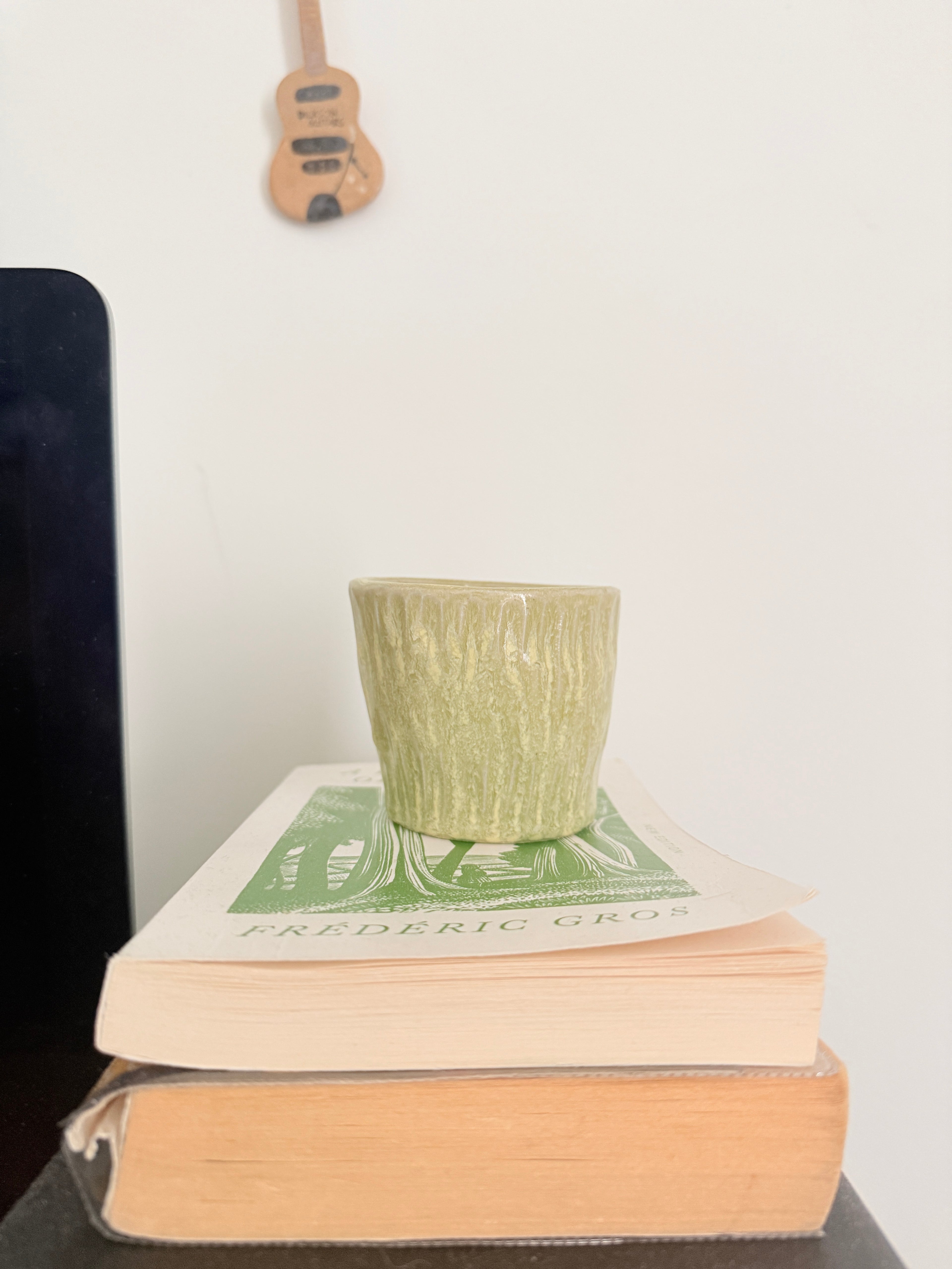 Green textured cup on a stack of books with a guitar in the background