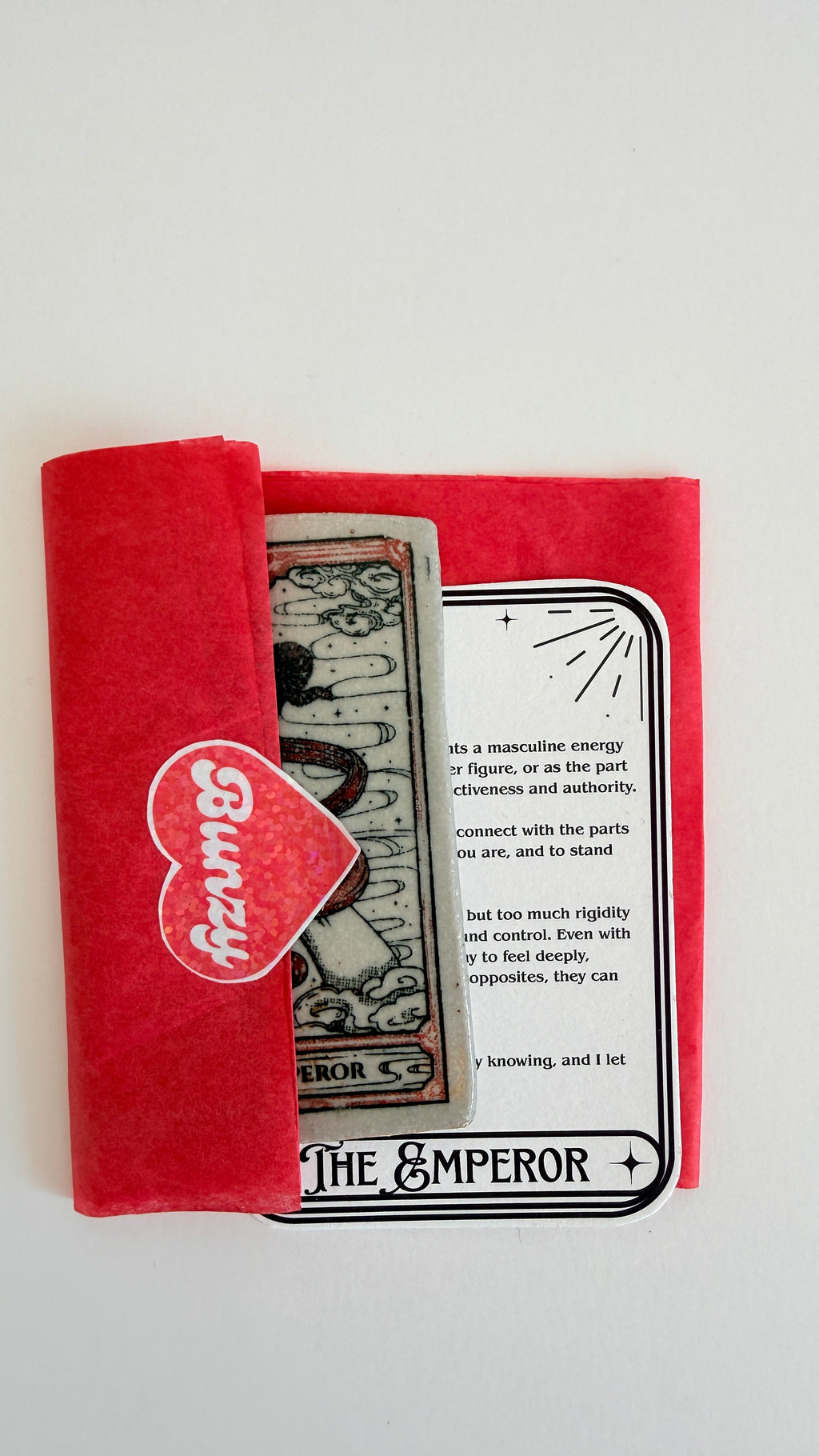 A red fabric card holder or wallet containing tarot cards, including 'The Emperor' card, photographed on a clean white background.