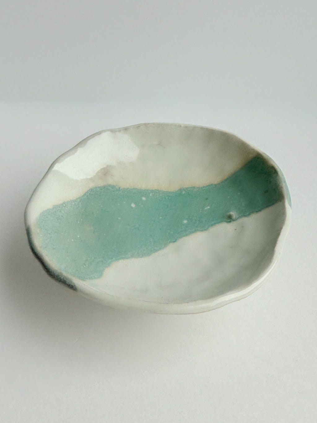 A handmade ceramic shallow bowl with an organic scalloped rim, featuring a glossy textured mint green glaze over a white clay base, set against a neutral light gray background.