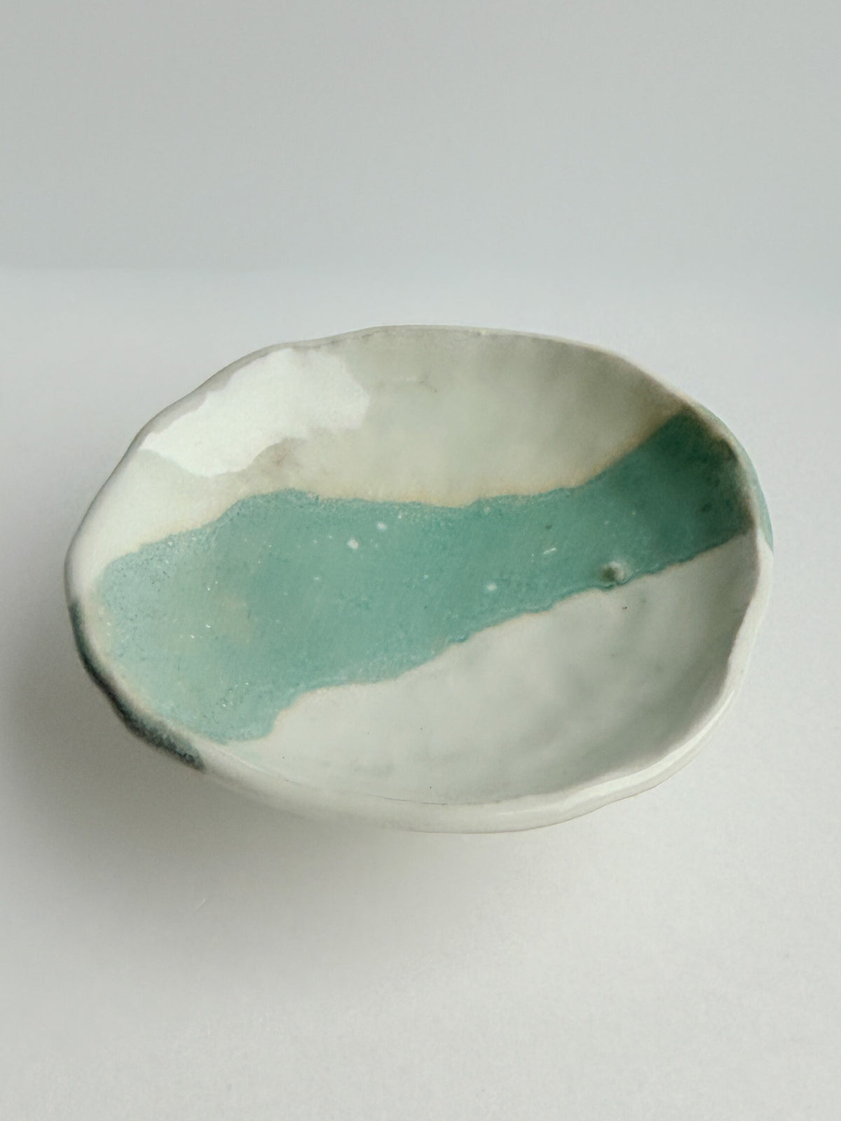 A handmade ceramic shallow bowl with an organic scalloped rim, featuring a glossy textured mint green glaze over a white clay base, set against a neutral light gray background.