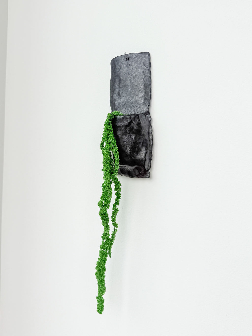 Large matte black handbuilt stoneware wall planter with trailing faux greenery hanging on a white wall