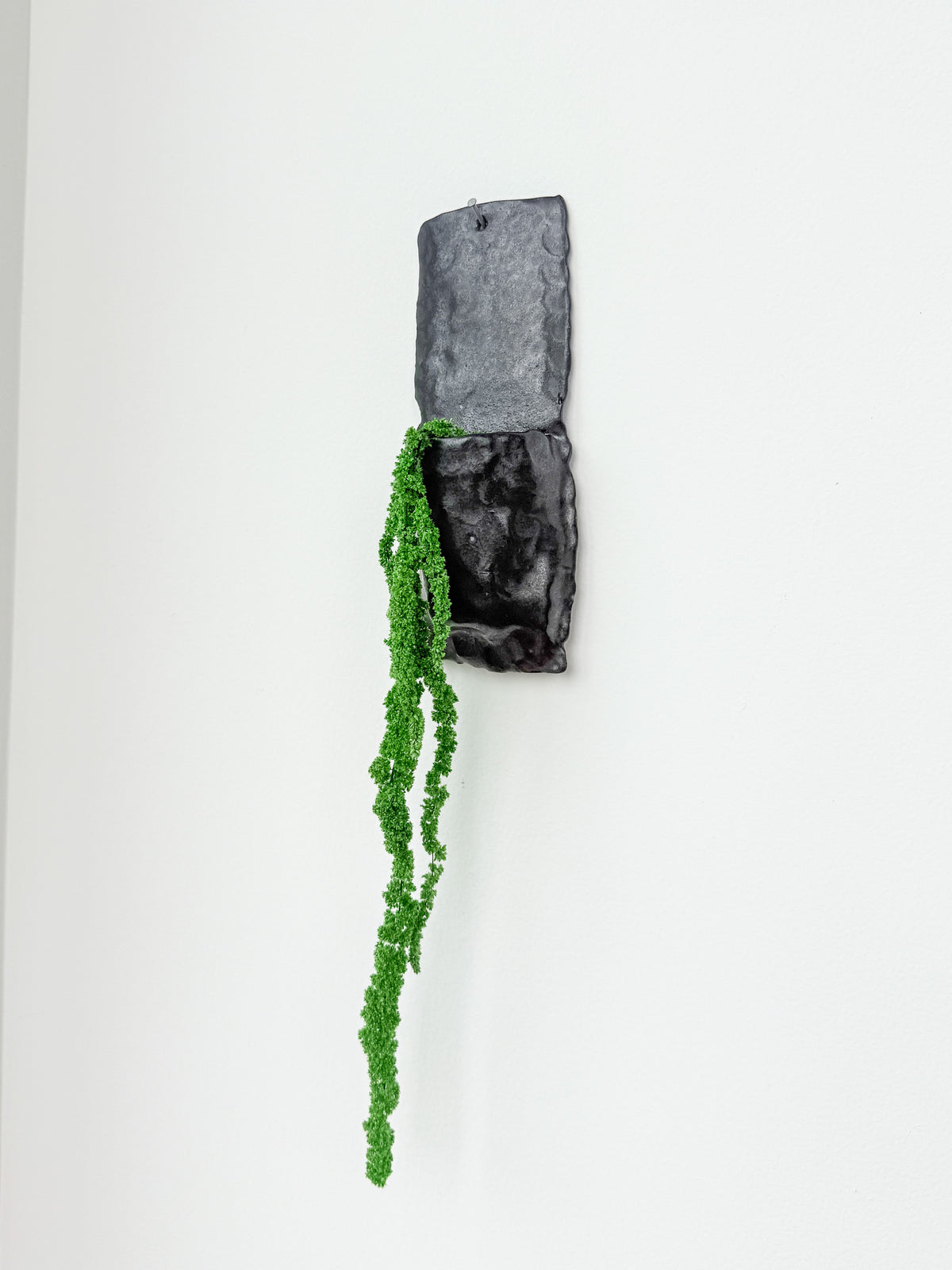 Large matte black handbuilt stoneware wall planter with trailing faux greenery hanging on a white wall