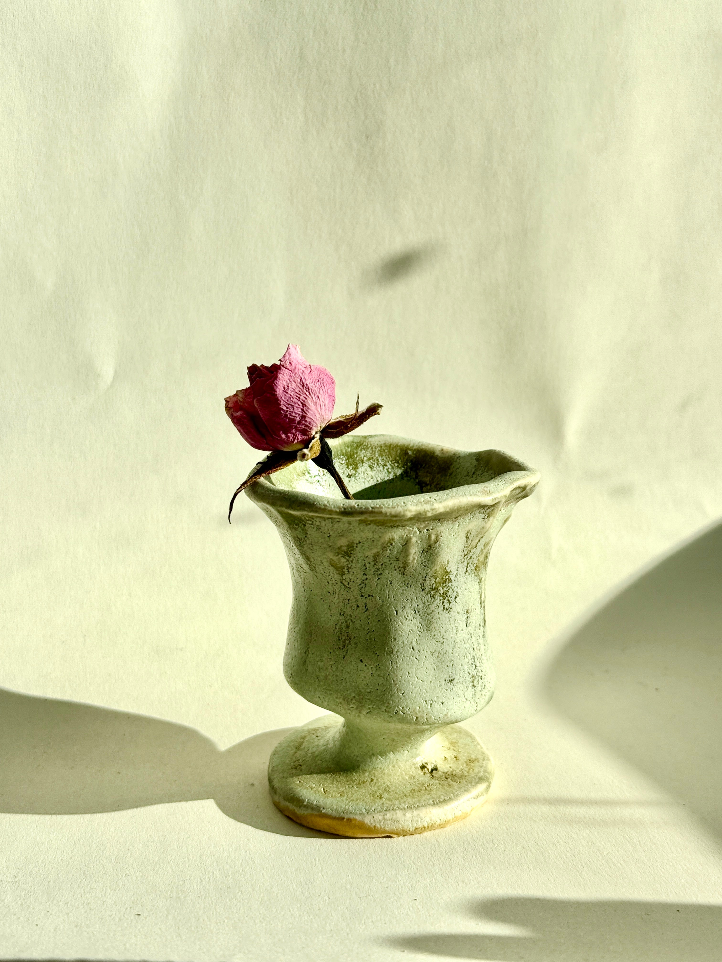 Green ceramic vase with a dried rose on a light background