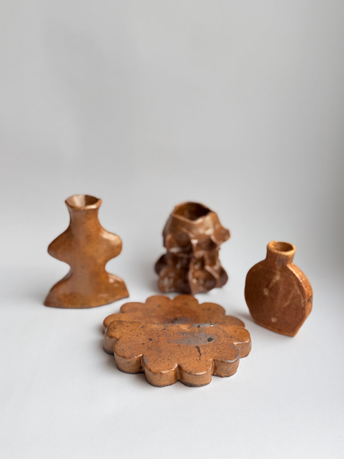 Four small rustic brown ceramic objects with organic, sculptural shapes arranged on a light gray studio background.