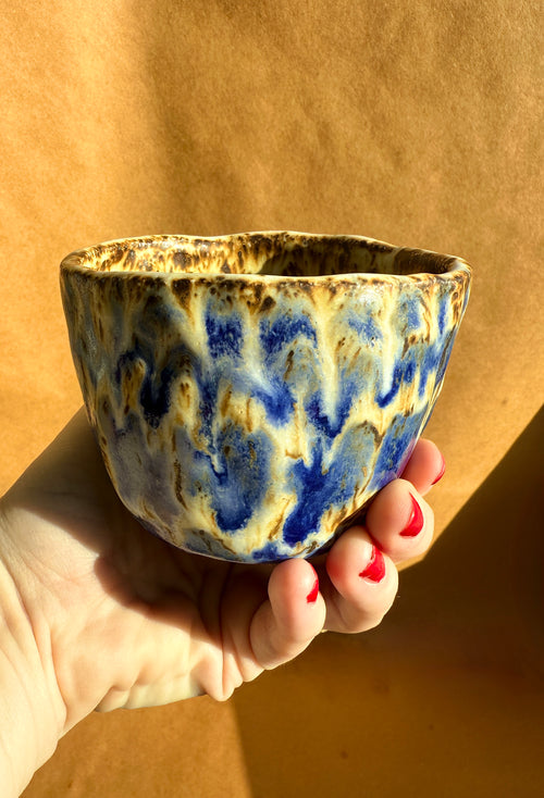Hand-built stoneware cup with flowing blue and earthy brown glaze, organic shape, held in hand - Bunzy NYC Ceramics