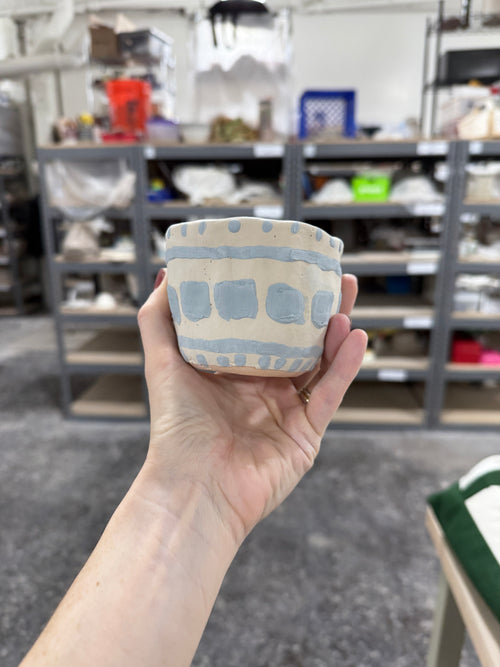 Hand-built stoneware cup with flowing blue and earthy brown glaze, organic shape, held in hand at studio before firing – Bunzy NYC ceramics
