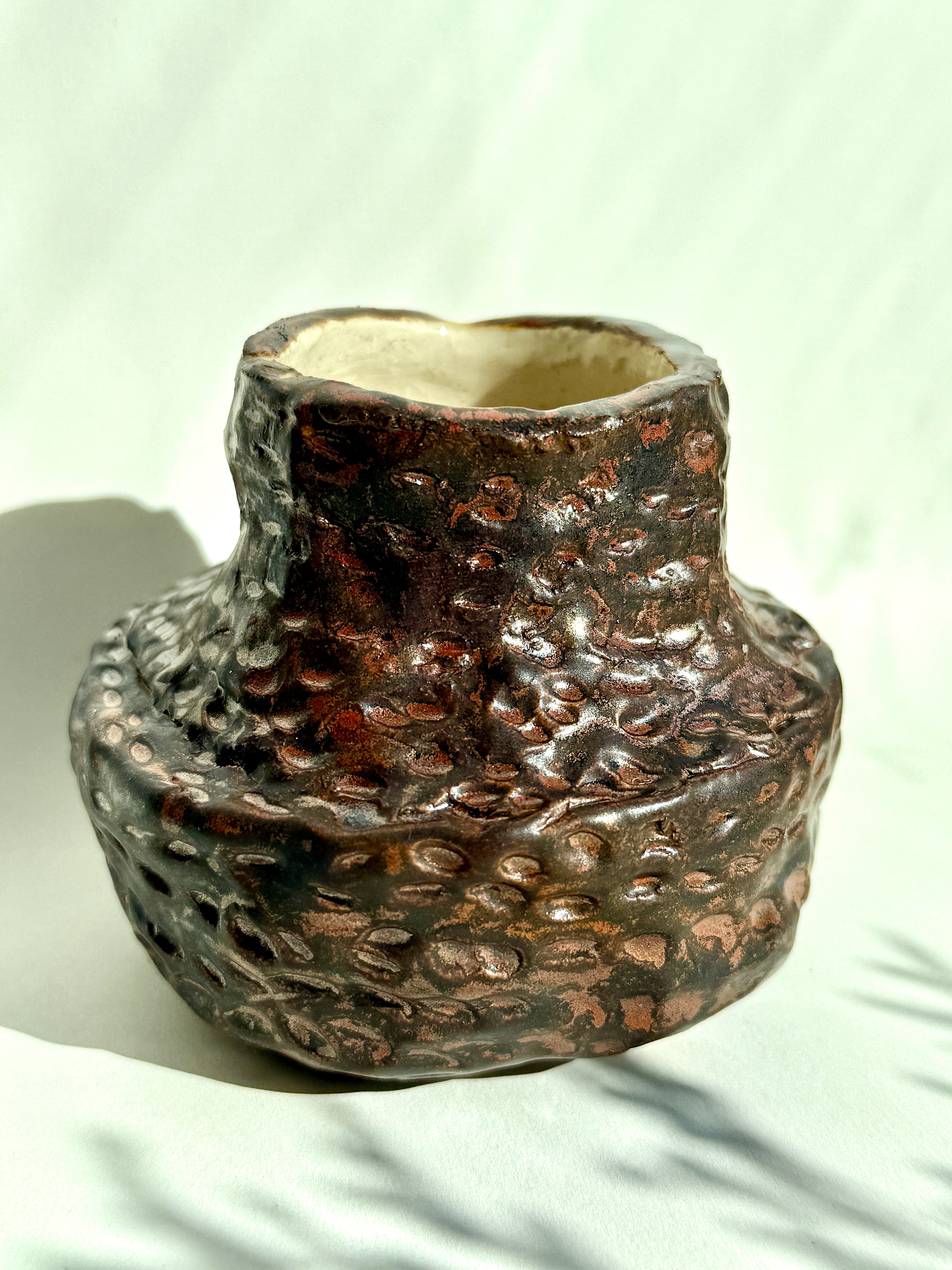 handbuilt textured stoneware vessel with cratered metallic glaze in natural light by Bunzy