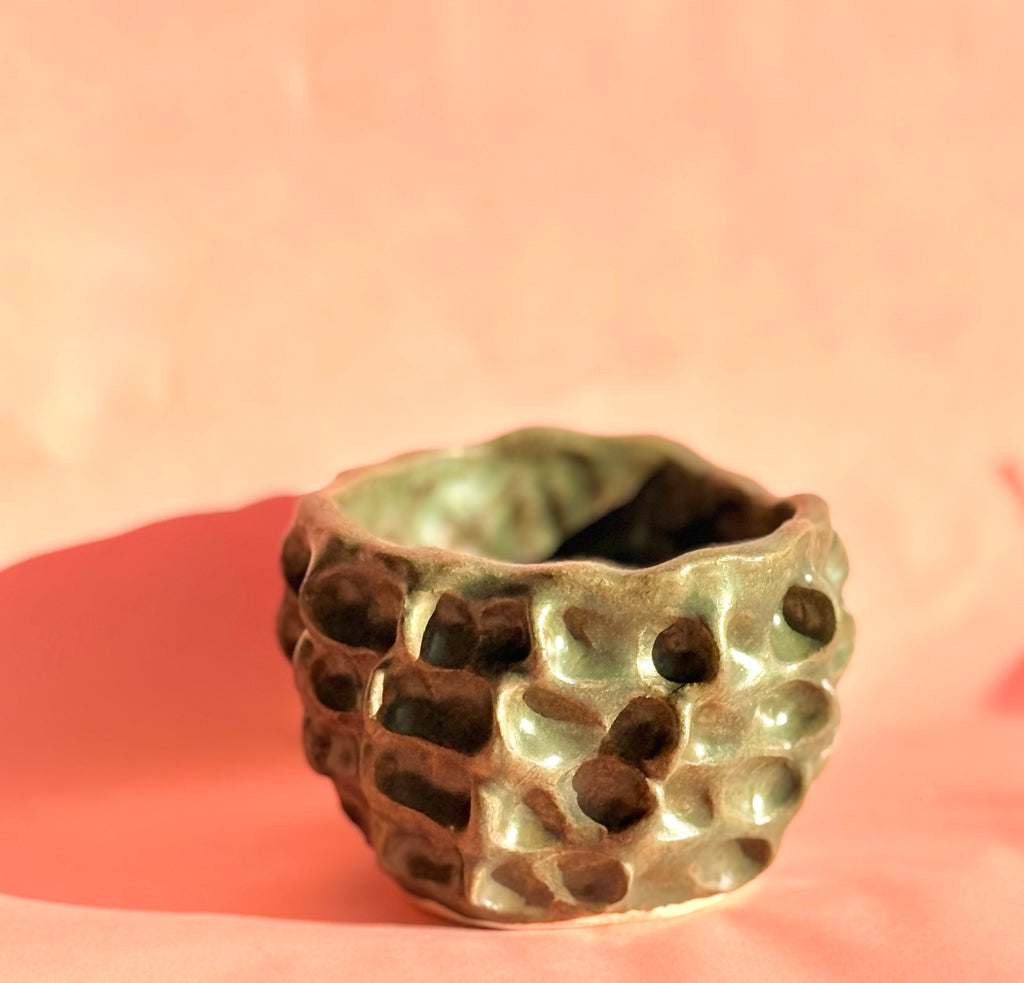 Hand built dimpled stoneware bowl with moss green glaze on pink background
