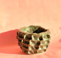 Hand built dimpled stoneware bowl with moss green glaze on pink background