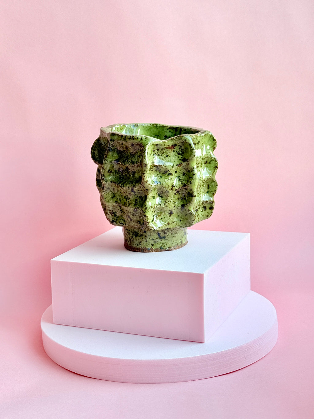 Green speckled handmade ceramic vase with sculptural texture on pink background