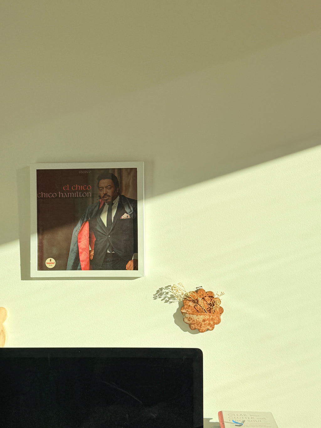 Framed album cover of 'Chico Hamilton' on a wall with a decorative flower arrangement.