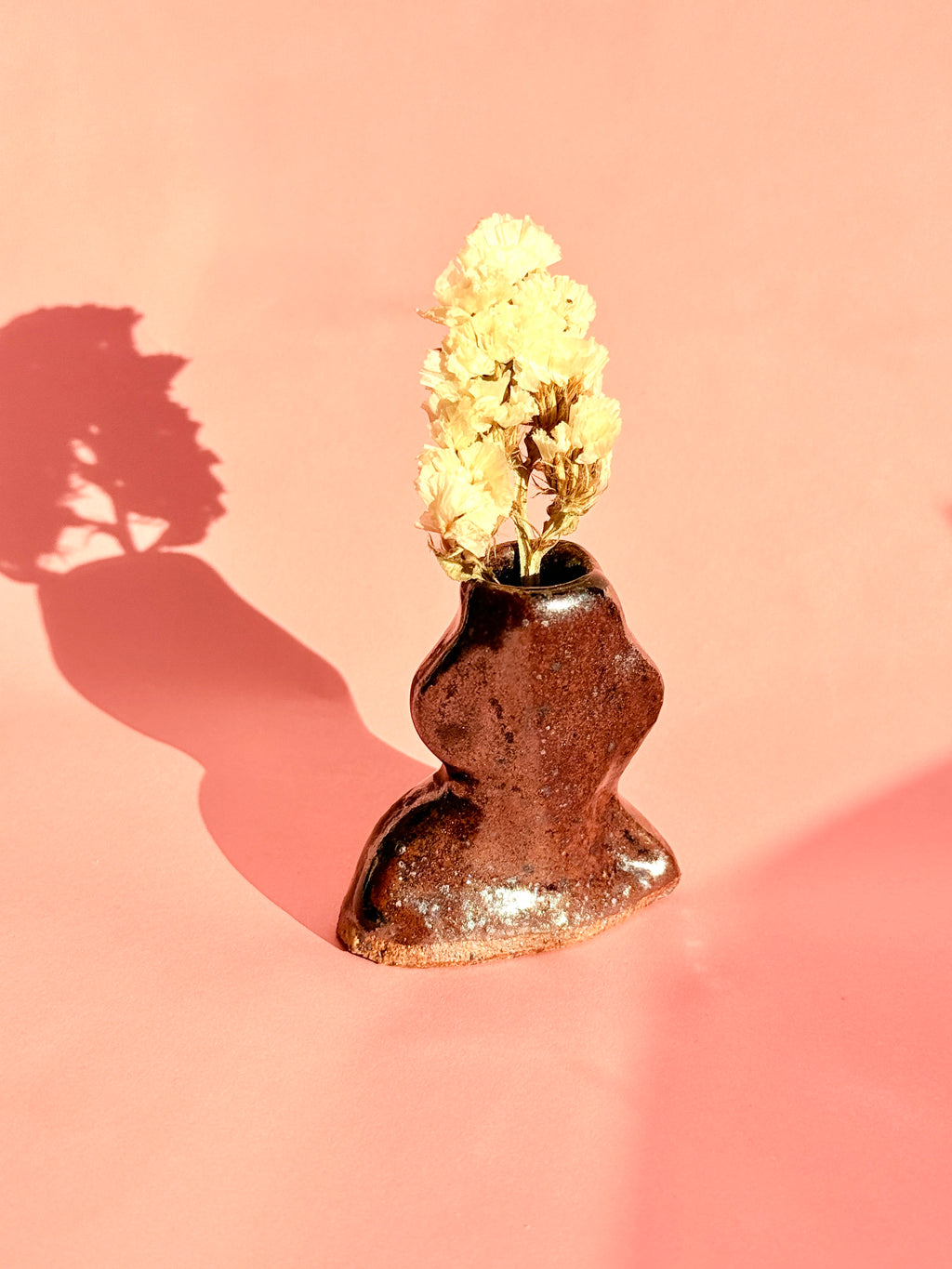 Small handmade rust brown ceramic bud vase holding dried flowers in studio light