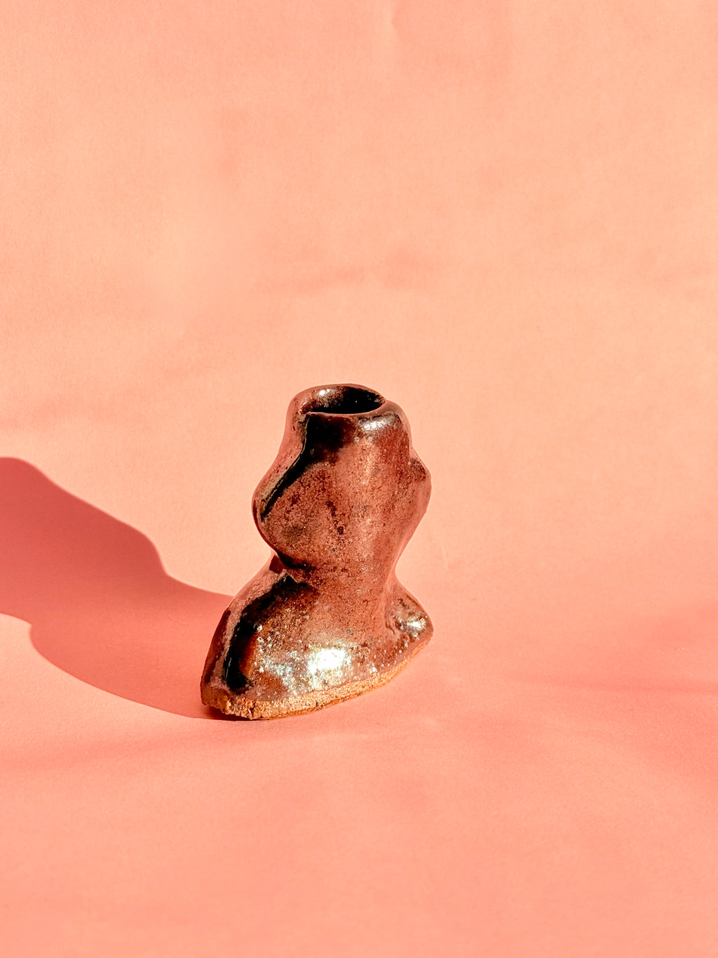 Handbuilt rust brown mini stoneware bud vase with organic sculptural shape on pink background
