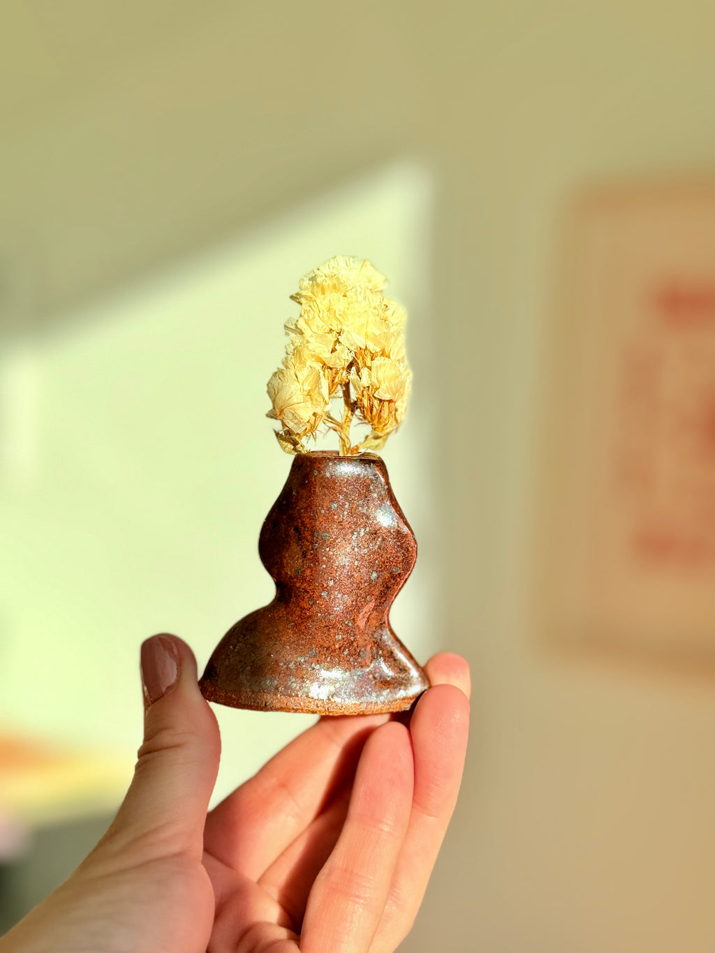 Hand holding a tiny rust brown sculptural ceramic bud vase with dried florals