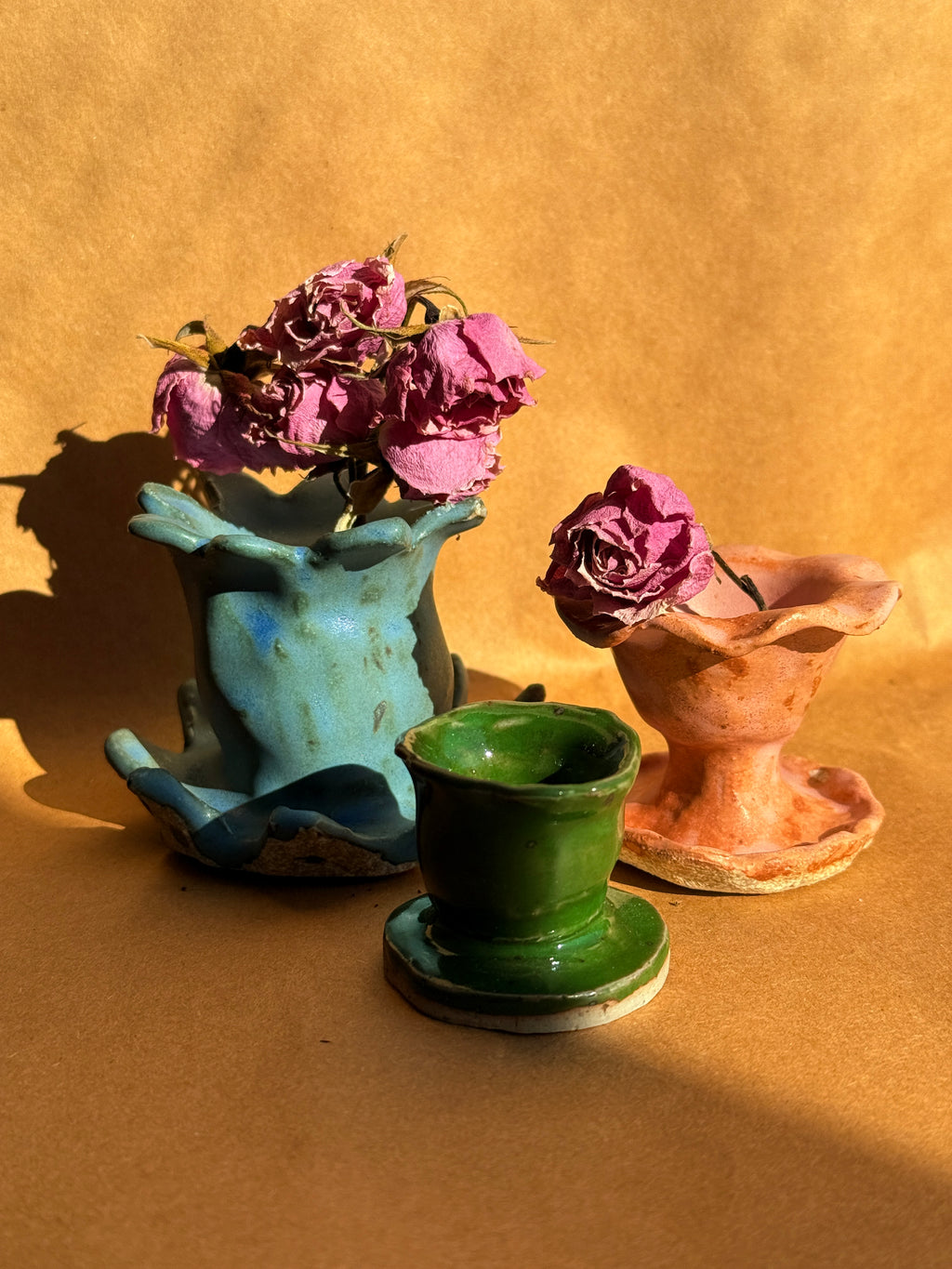 Hand-built stoneware pink pedestal incense cone holder with sculptural ruffled edges and organic form, pictured with two other ceramic items