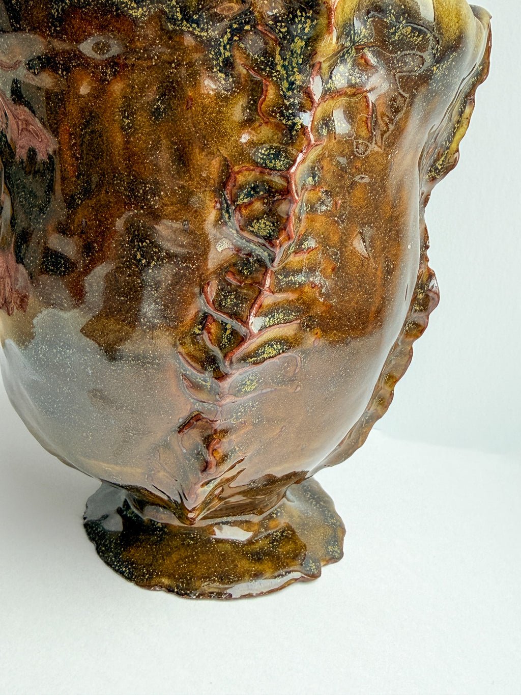 A close-up of a sculptural ceramic vase with a glossy, organic, organic-like glaze in earthy brown, amber, and gold tones with subtle yellow and green marbling.