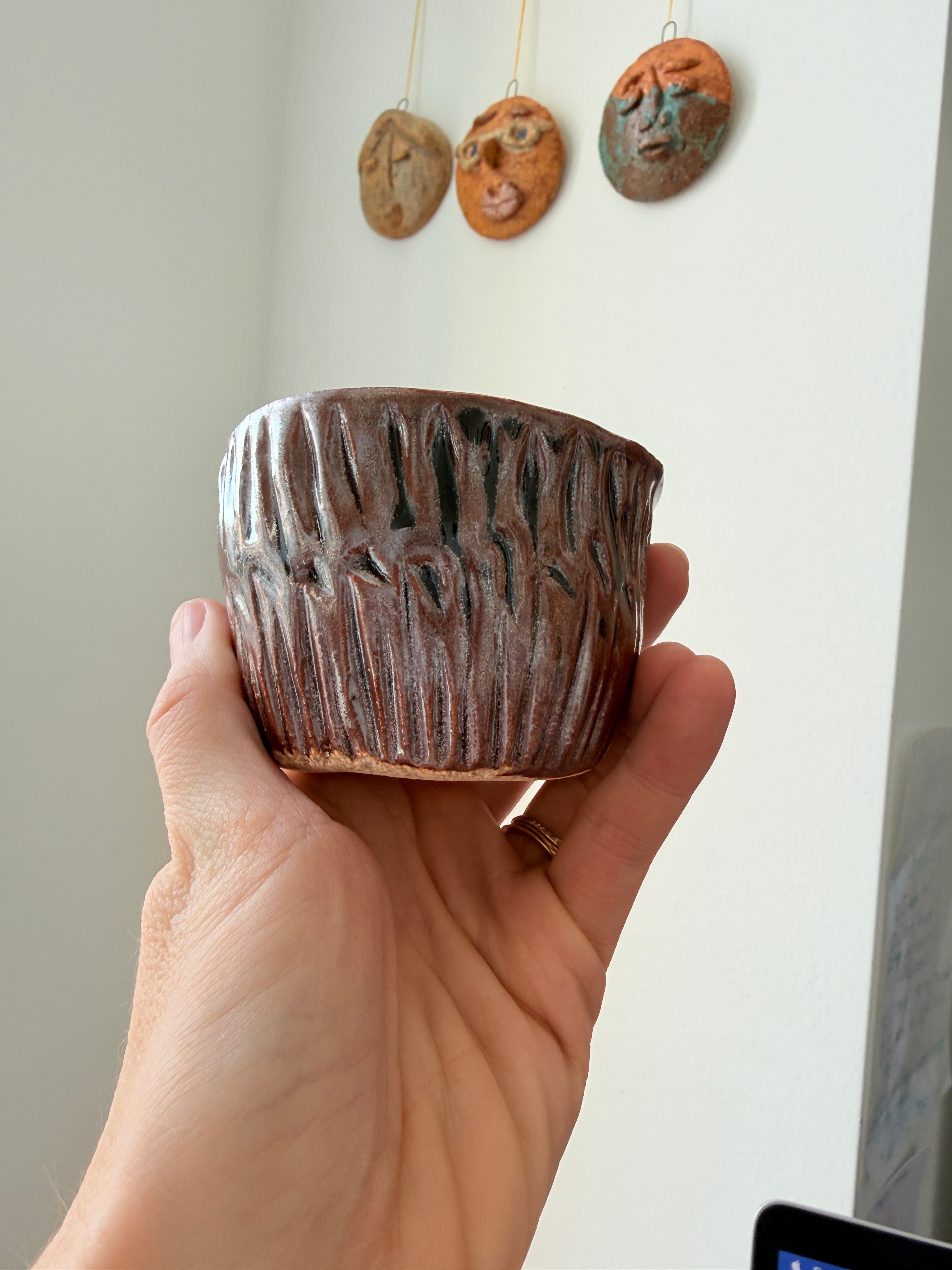 Hand holding a textured ceramic object with three similar items on a white surface