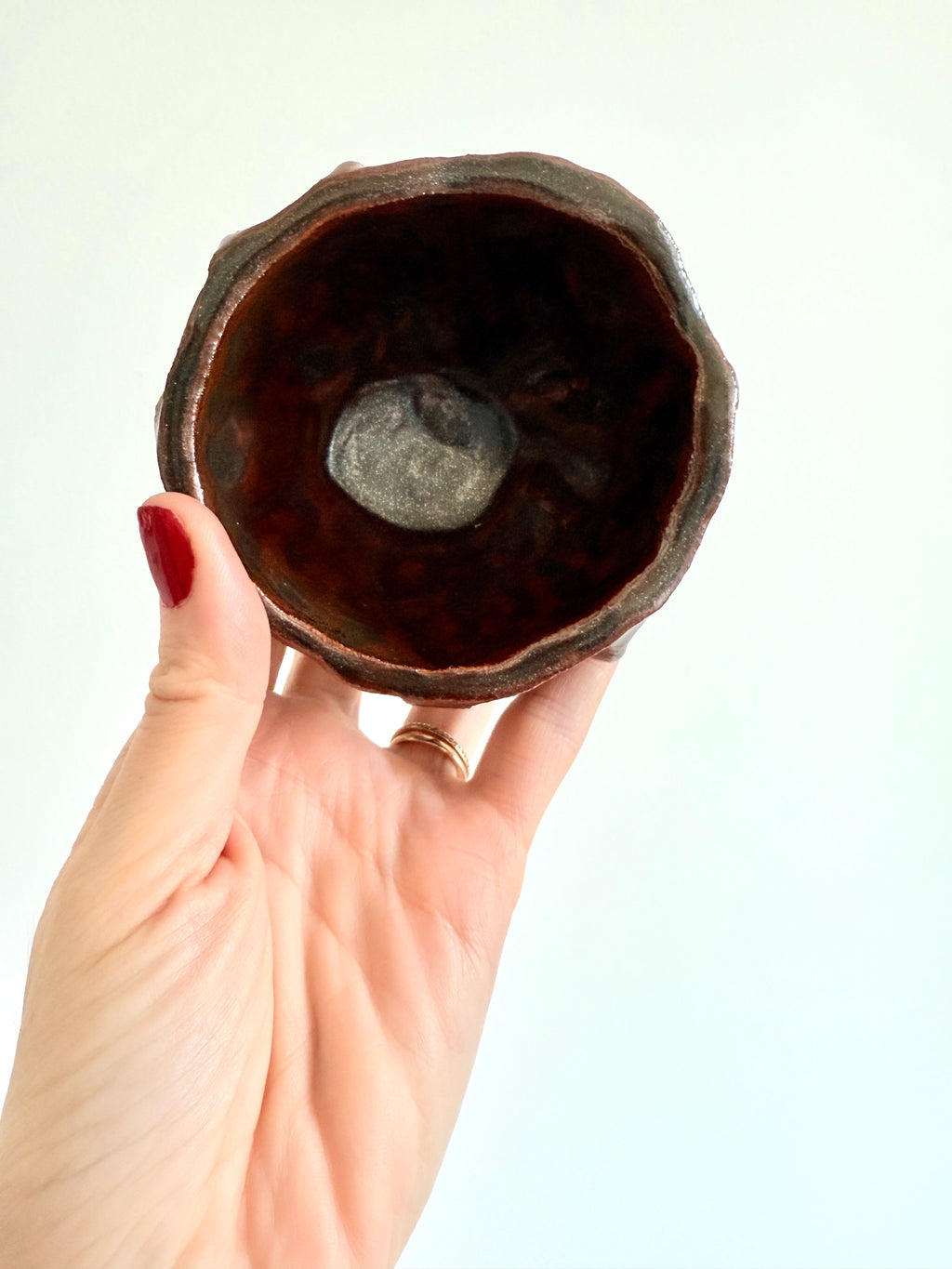 Hand-built stoneware cup with earthy brown glaze, organic shape, held in hand
