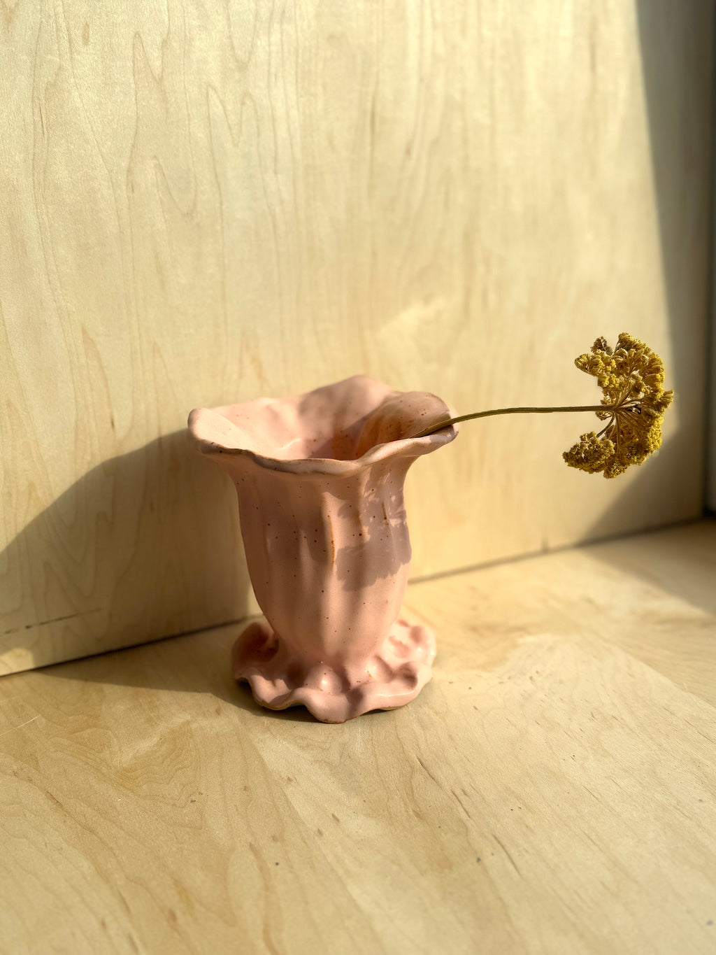 Pink ceramic vase with a single dried flower on a wooden surface