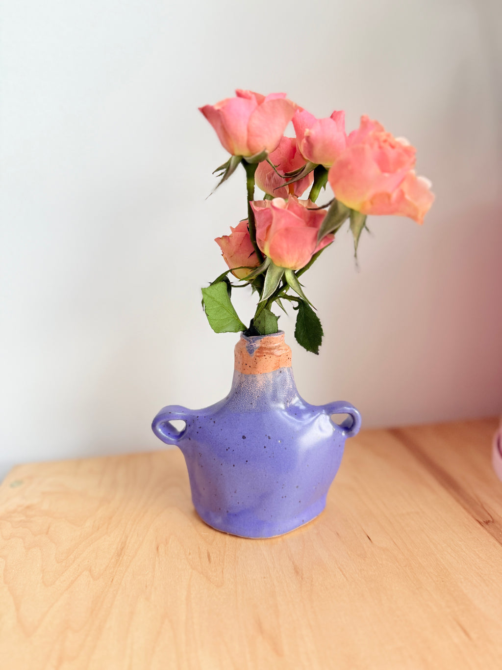 Hand-built stoneware bud vase with soft lavender glaze, speckled surface, and small side handles holding pink flowers