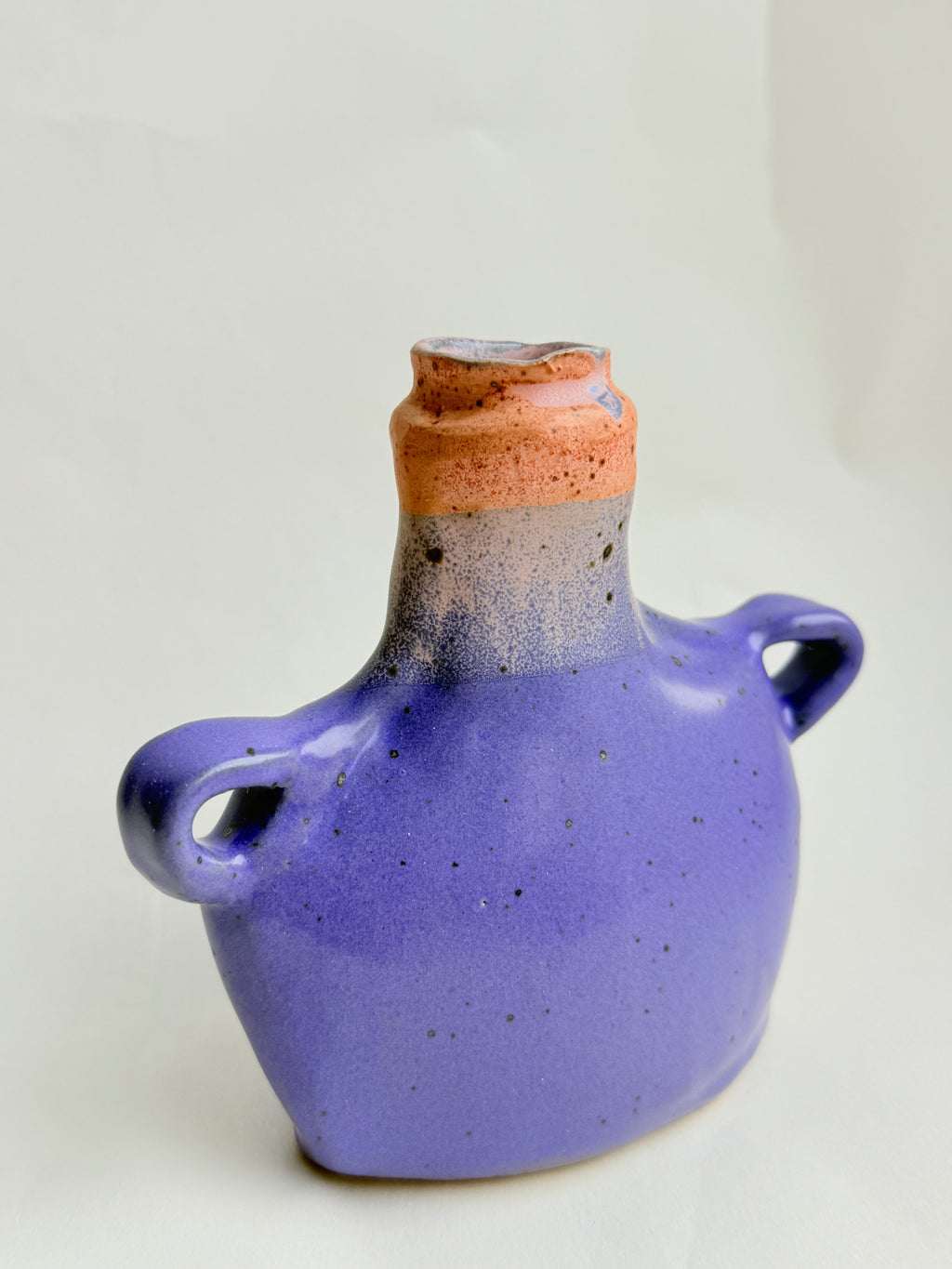 Hand-built stoneware bud vase with soft lavender glaze and pink rim, speckled surface, and small side handles 