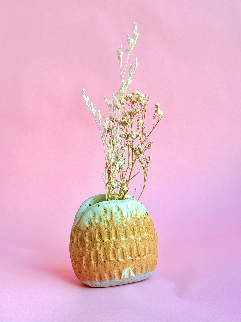 Ceramic vase with textured surface and dried plants on a pink background