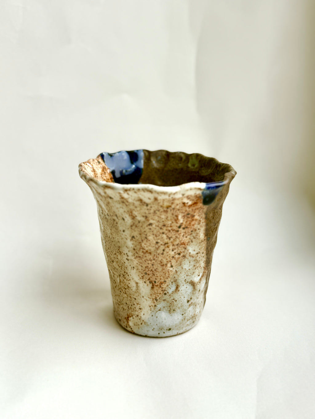 Hand-built stoneware cup with creamy speckled glaze and subtle blue