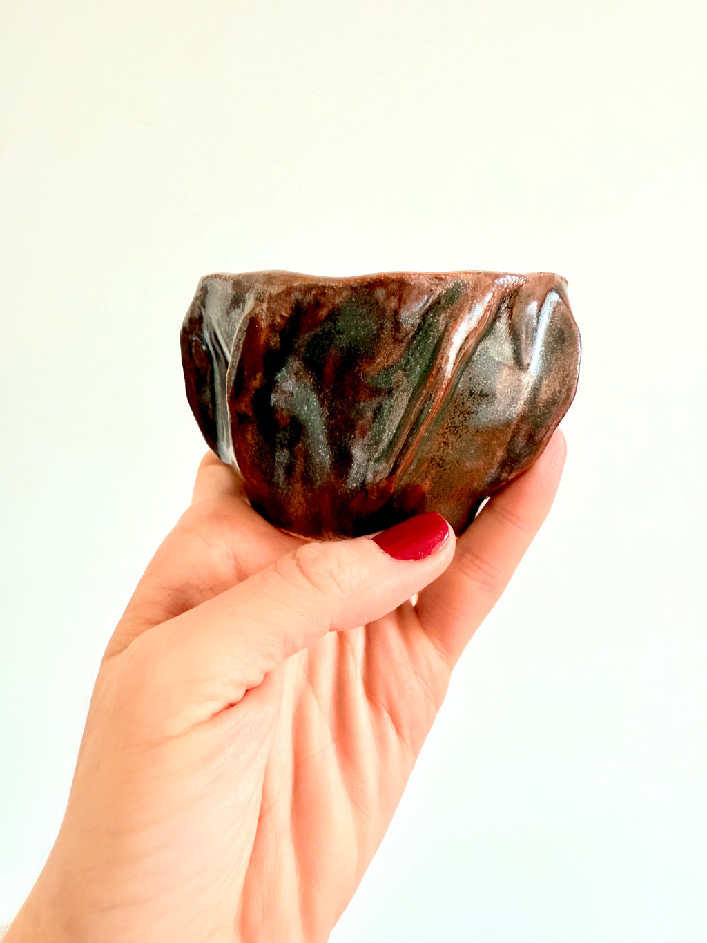 Hand-built stoneware cup with earthy brown  glaze, organic shape, held in hand